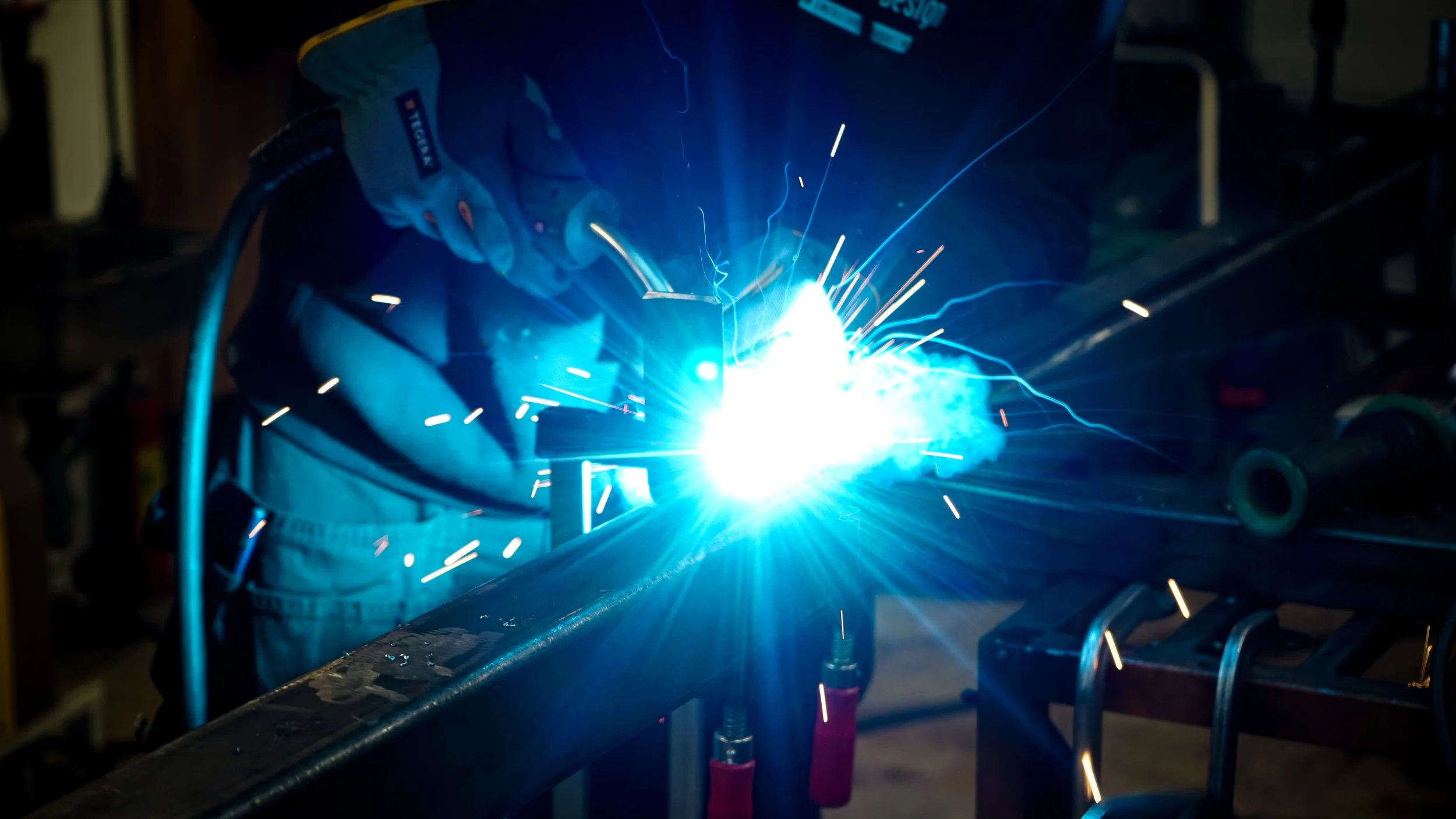 Person svetsar med ljusblixt och gnistor i ett verkstad eller workshop.
