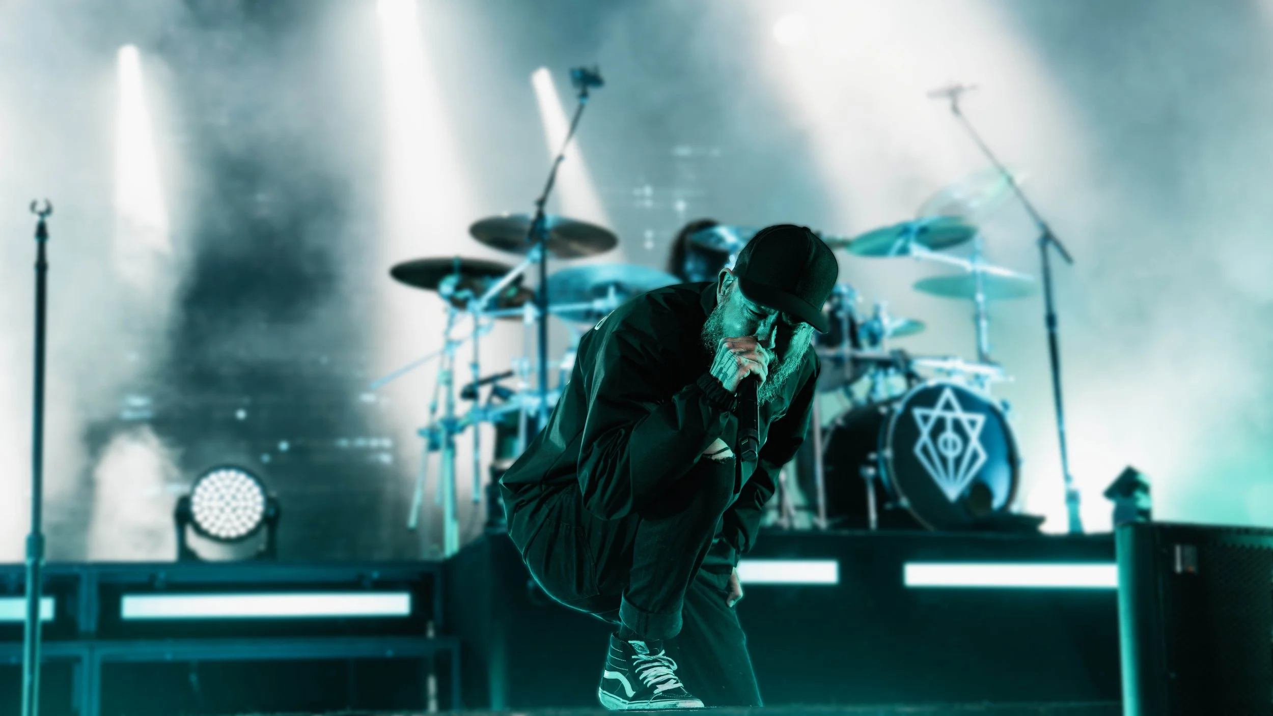 En man som sjunger i en mikrofon på scenen under en musikshow, med ett trumset i bakgrunden.