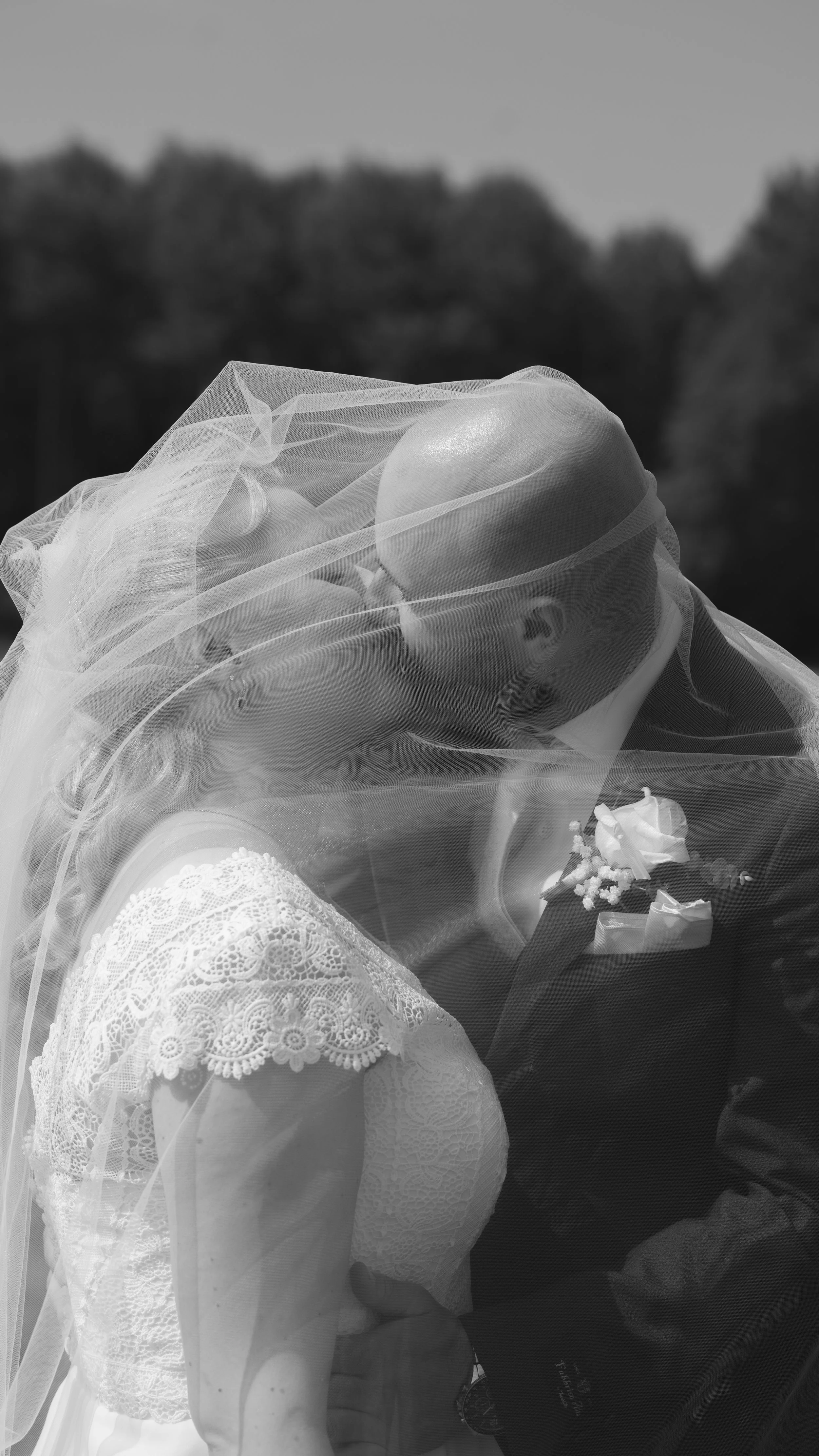 En brud och en brudgum som kysser varandra under en bröllopsfotografering, omslutna av en genomskinlig brudslöja.