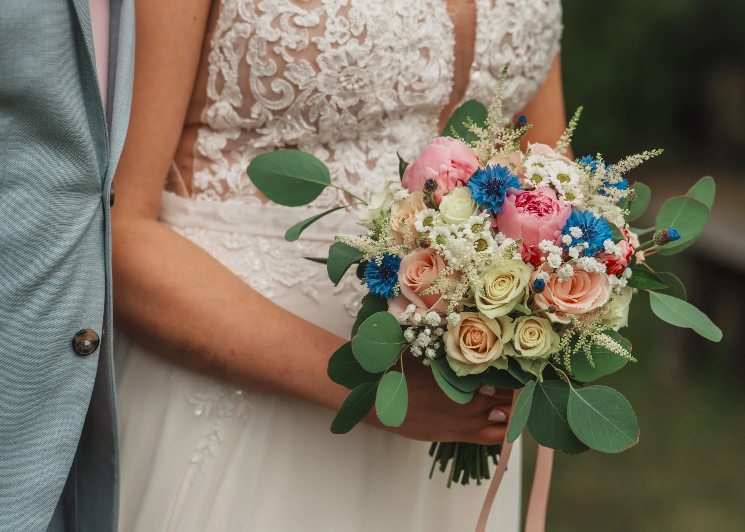 Brudens hand håller en bukett med rosa, vit, blåa blommor och gröna blad, efter ett bröllop.