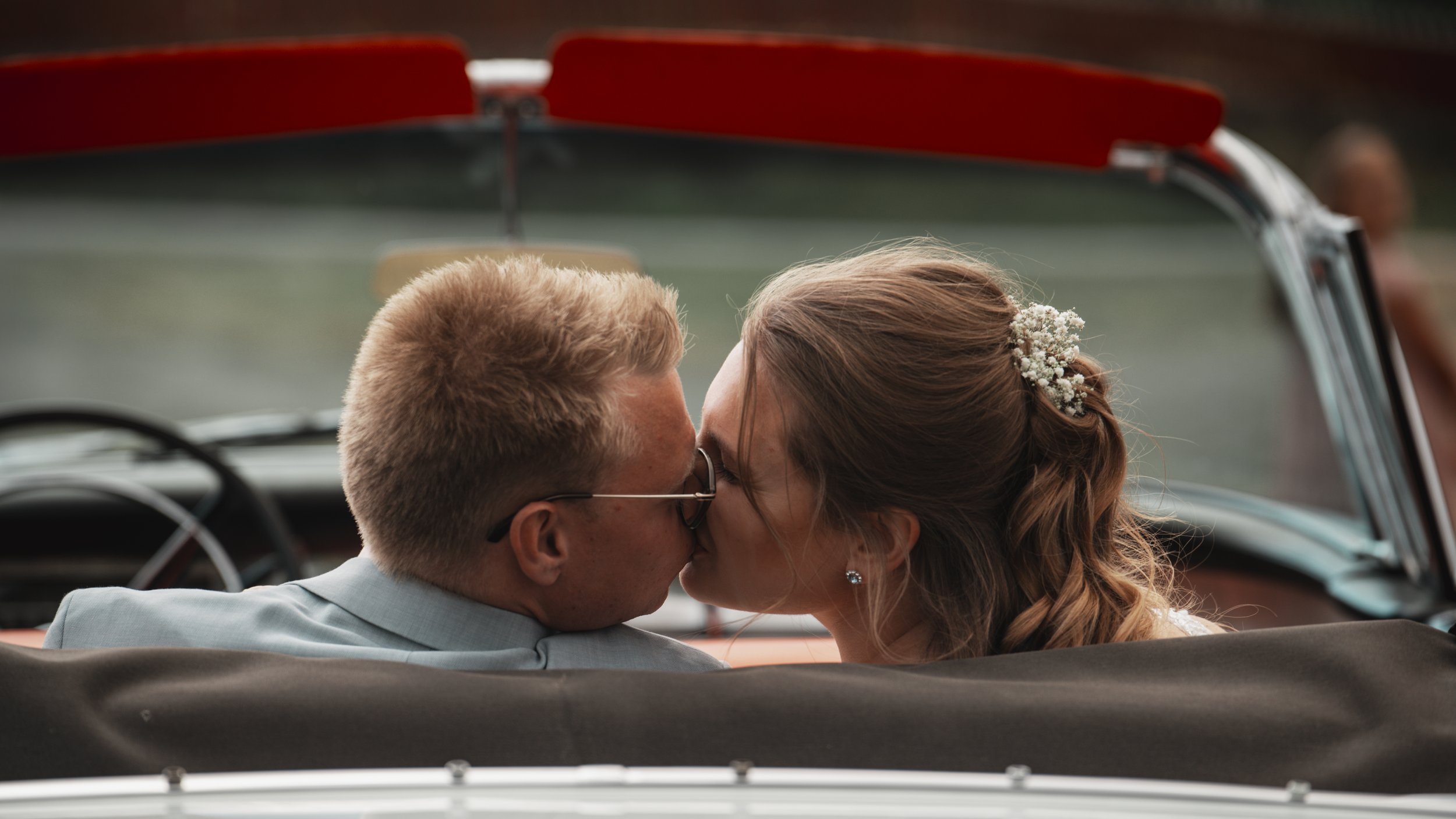 En nygift man och kvinna kyssas i en bil, som ser ut att vara ett bröllopsfoto.