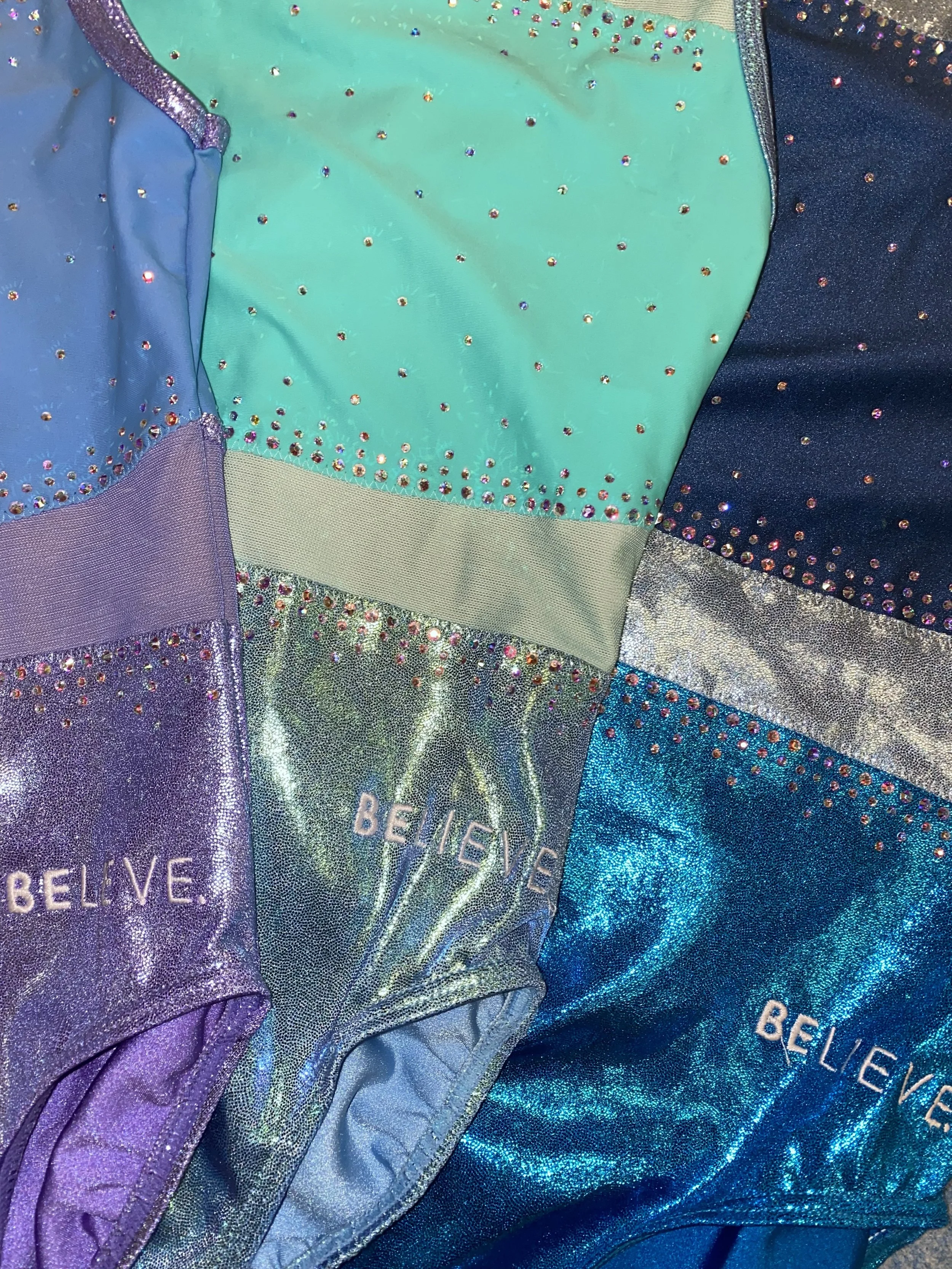 Close-up of a patchwork fabric with various shiny, rainbow-colored and metallic sections, some embroidered with the word "BELIEVE."