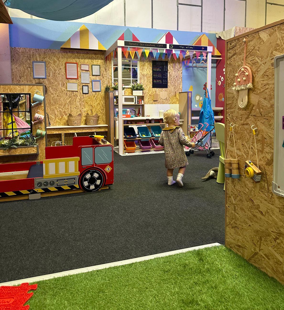 A young girl playing in a colorful indoor play area with a farm-themed decor and various toy structures.