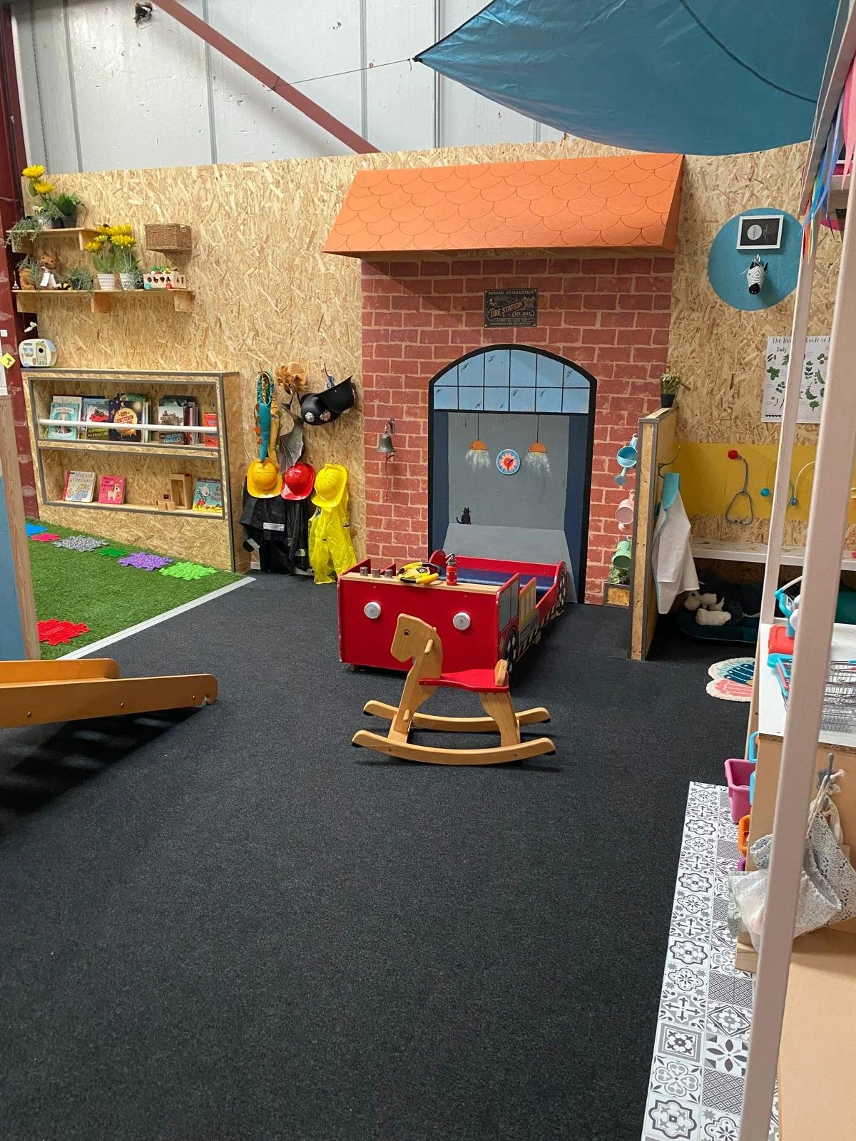 Colorful indoor children's play area with a pretend house, wooden rocking horse, and various toys and decorations.