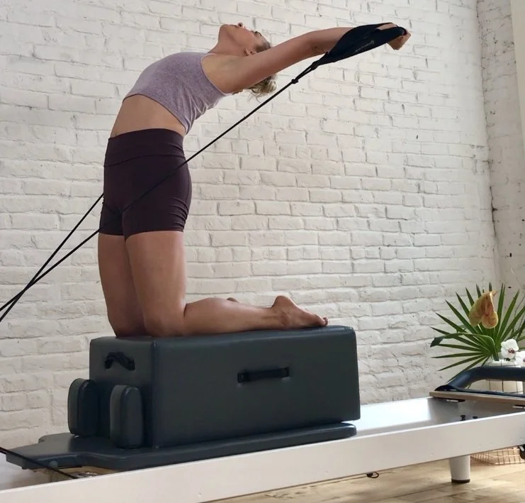 A woman practicing yoga on a reformer machine in a studio with a white brick wall.