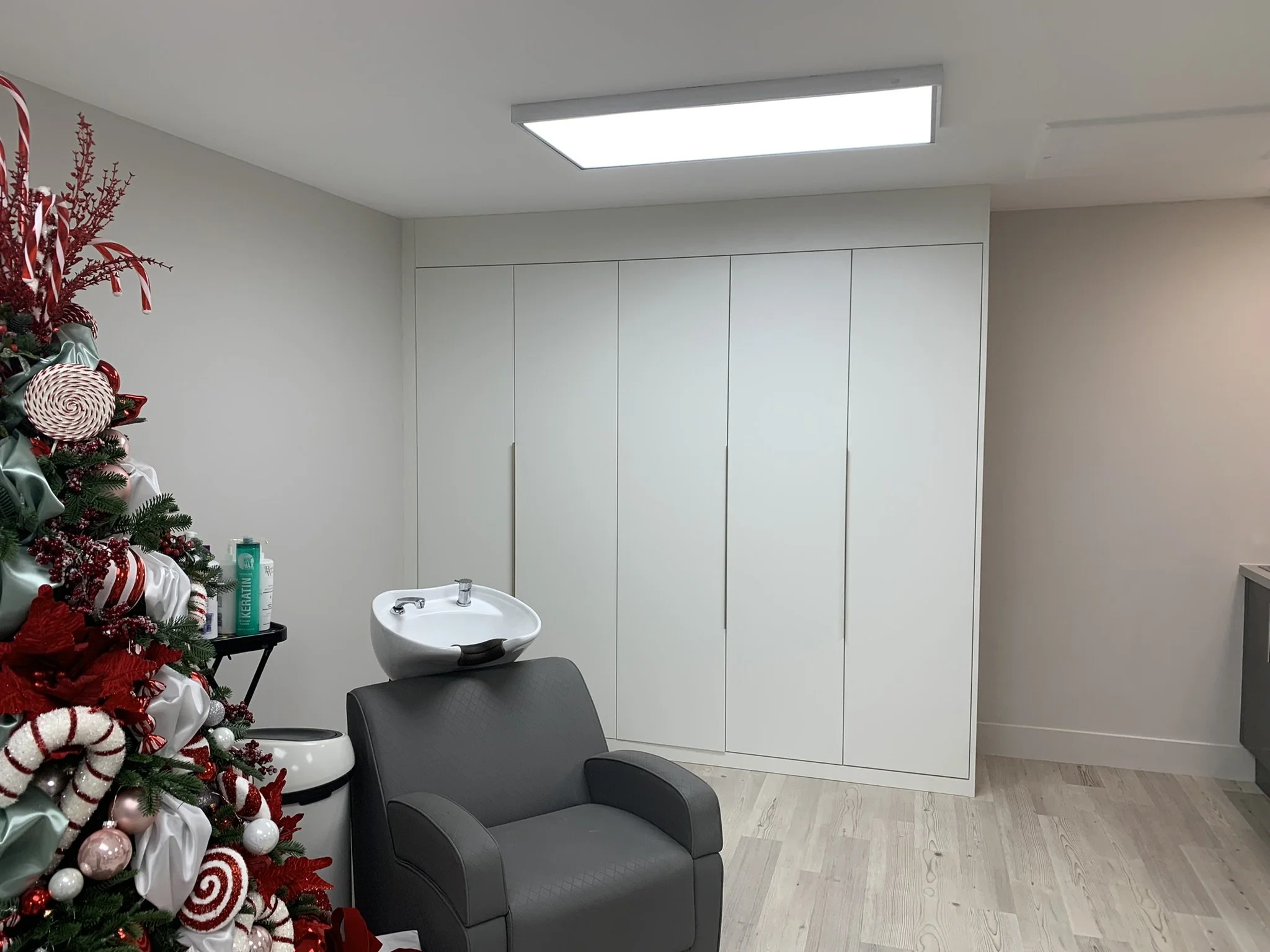 Salon interior with Christmas decorations, featuring a gray salon chair, a white washing basin, and a Christmas tree with red and white ornaments.