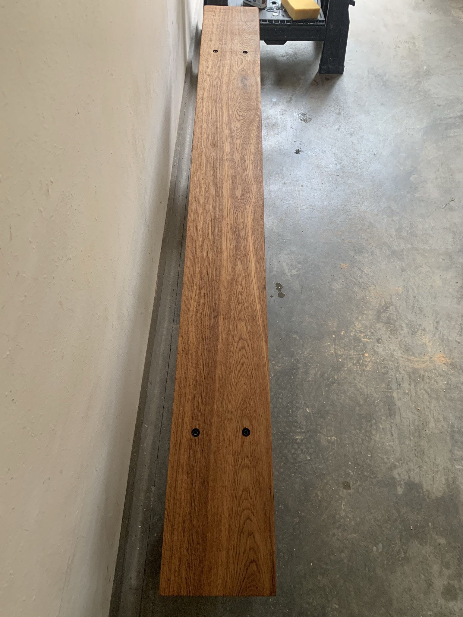 Long wooden board with visible grain pattern placed against a wall in a garage setting.