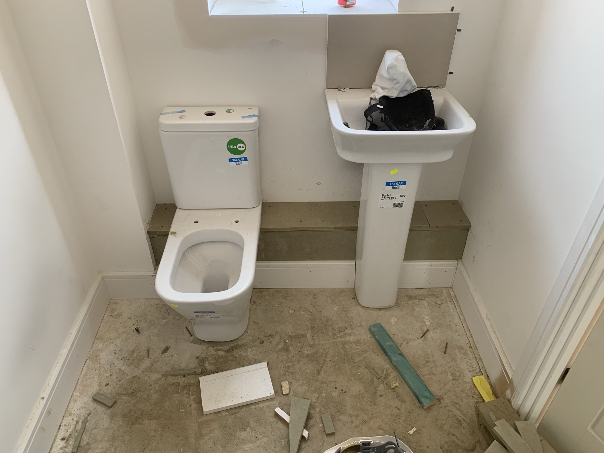Under-construction bathroom with toilet, sink, and building materials on the floor.