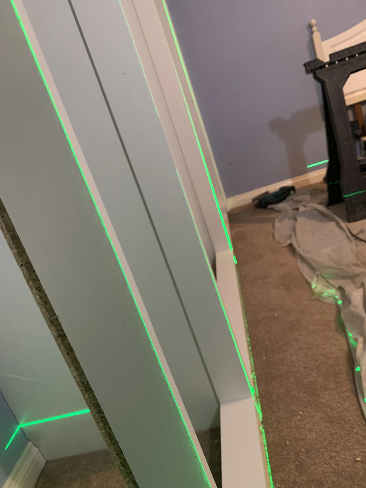 Vertical boards lined with green laser level lines in a room with partially visible furniture and floor covering.