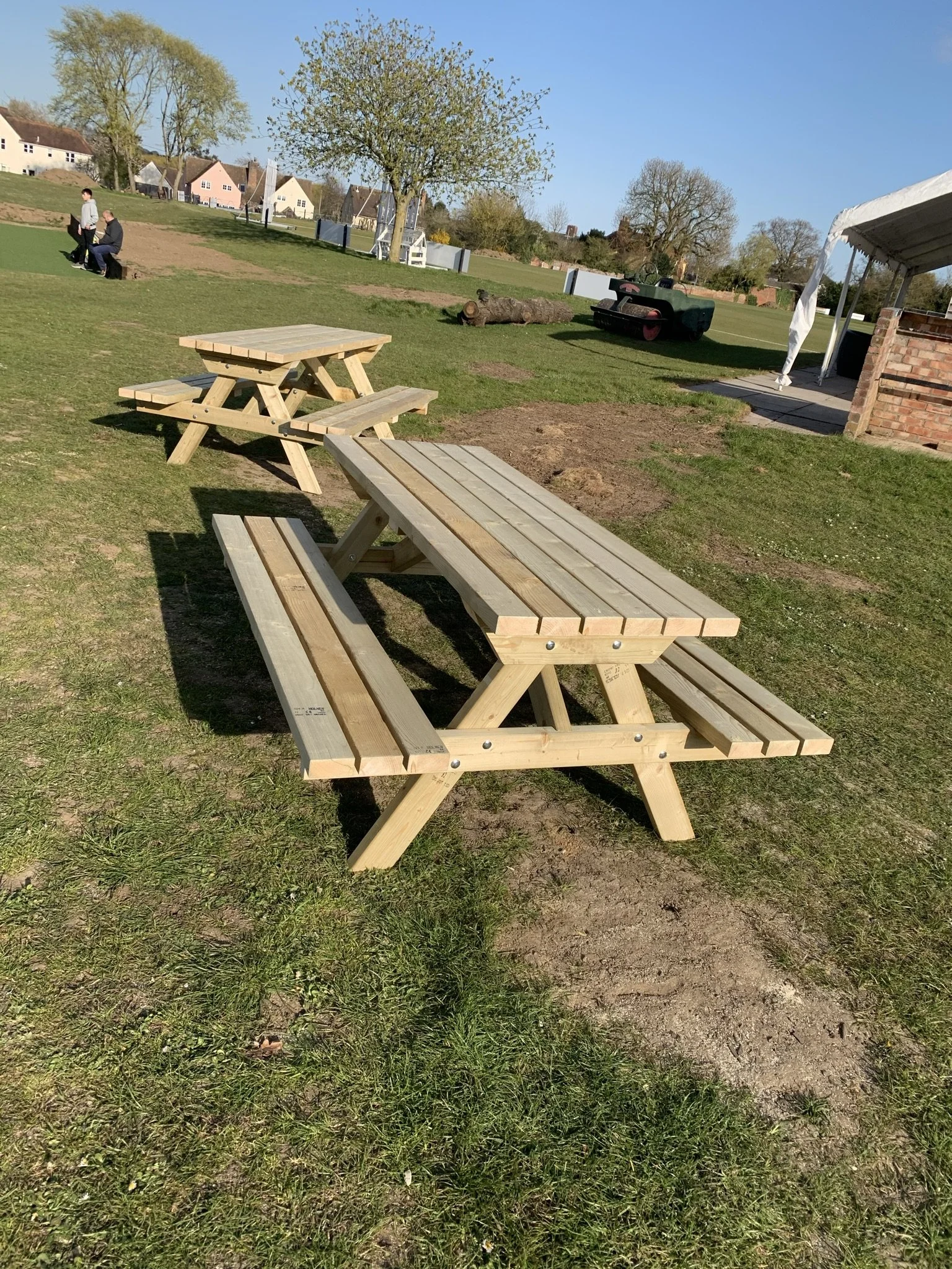 Outdoor picnic tables on grass with people in the background on a sunny day.