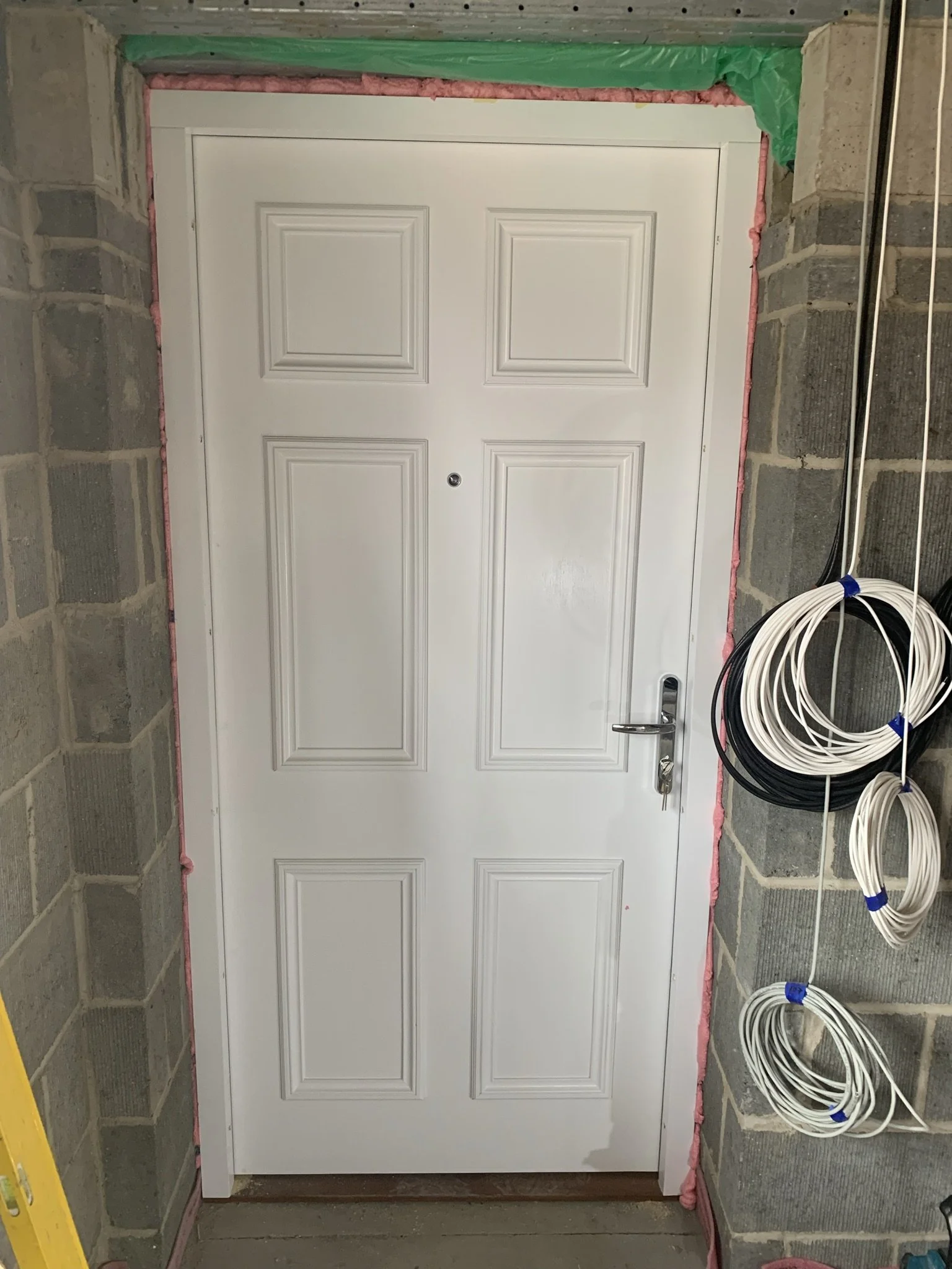 White door with silver handle, surrounded by brickwork, insulation, and coiled cables on the right.