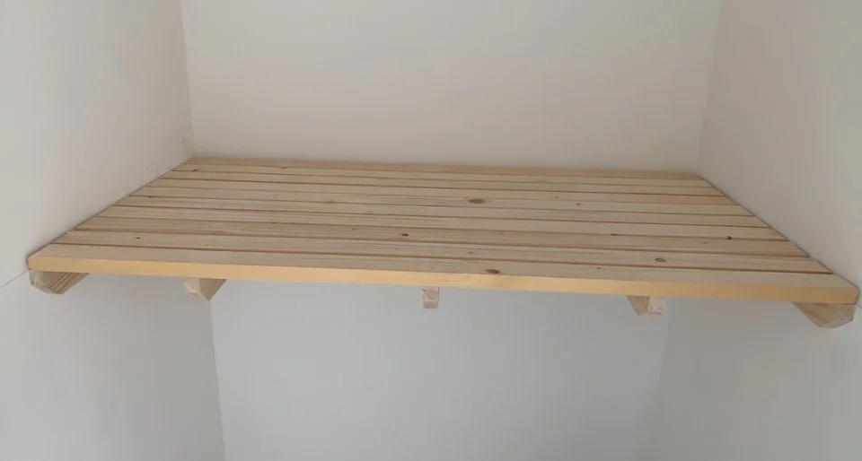 Wooden shelf installed in a corner on a white wall.