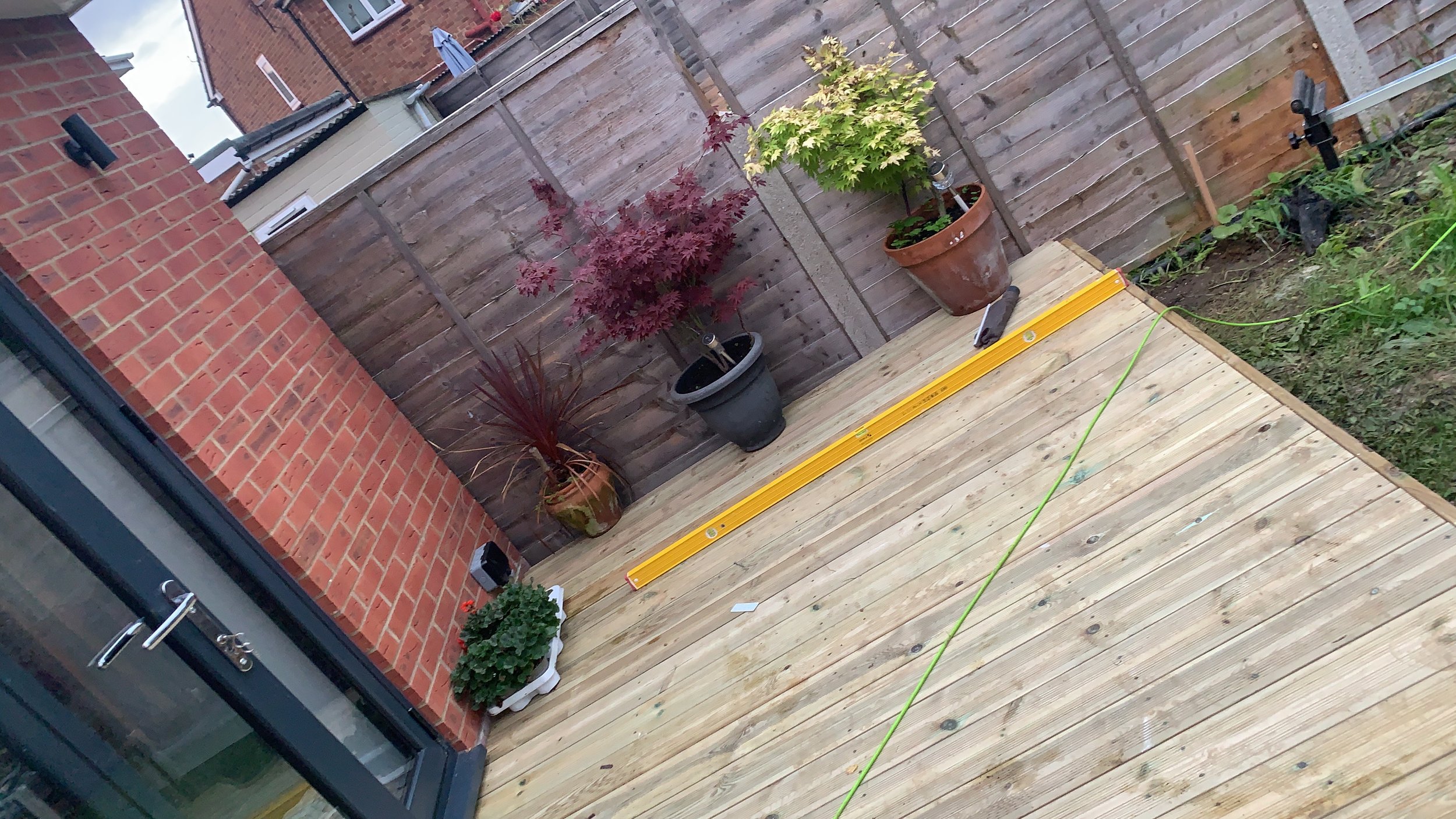 Wooden deck with potted plants, brick wall, and a wooden fence in a backyard setting.