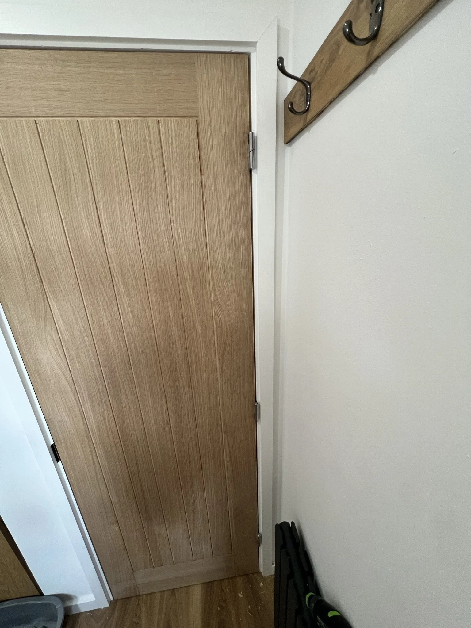 Wooden door with vertical grooves, adjacent coat rack on wall with hooks, light-colored walls and floor.