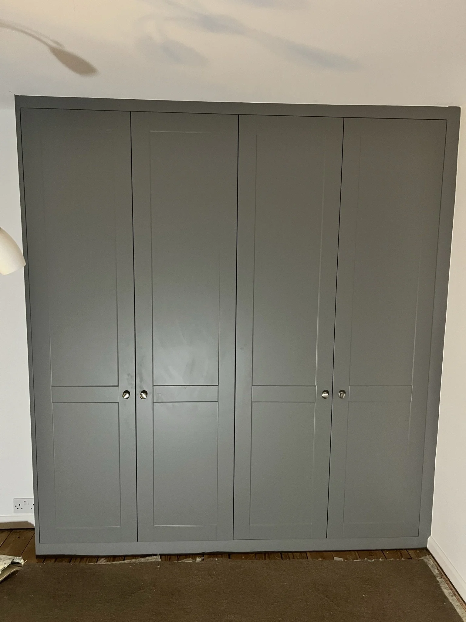 Gray wardrobe with four paneled doors and silver handles in a room.
