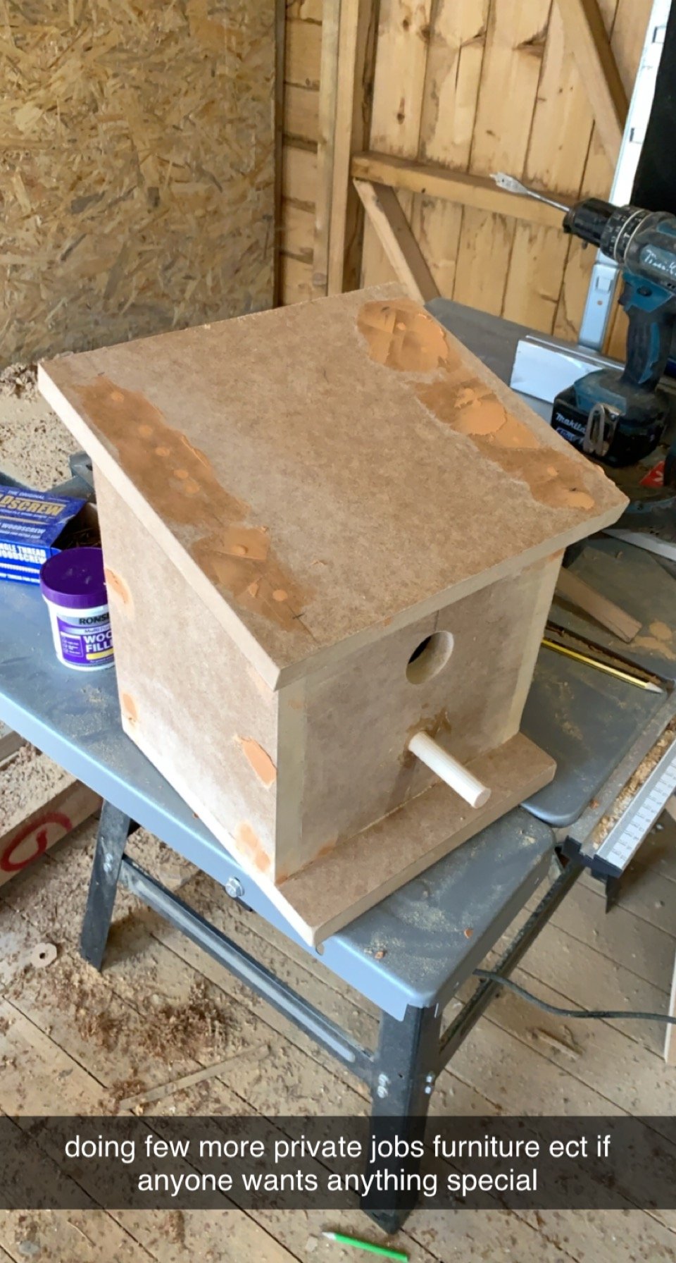 Wooden birdhouse under construction on a workbench, with wood filler and tools in a workshop.