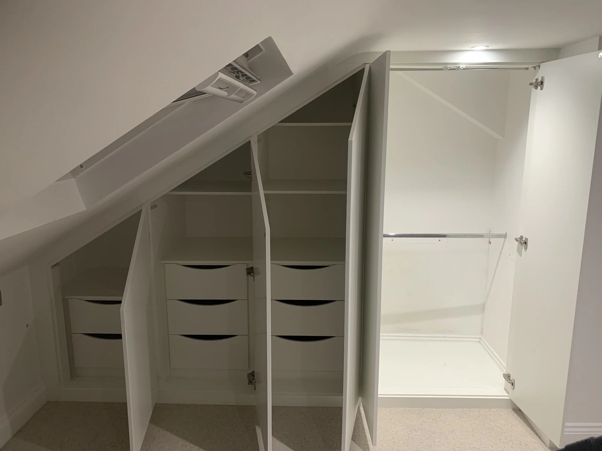 White built-in closet with open doors, several shelves, and drawers. The closet is designed to fit under a sloped ceiling.