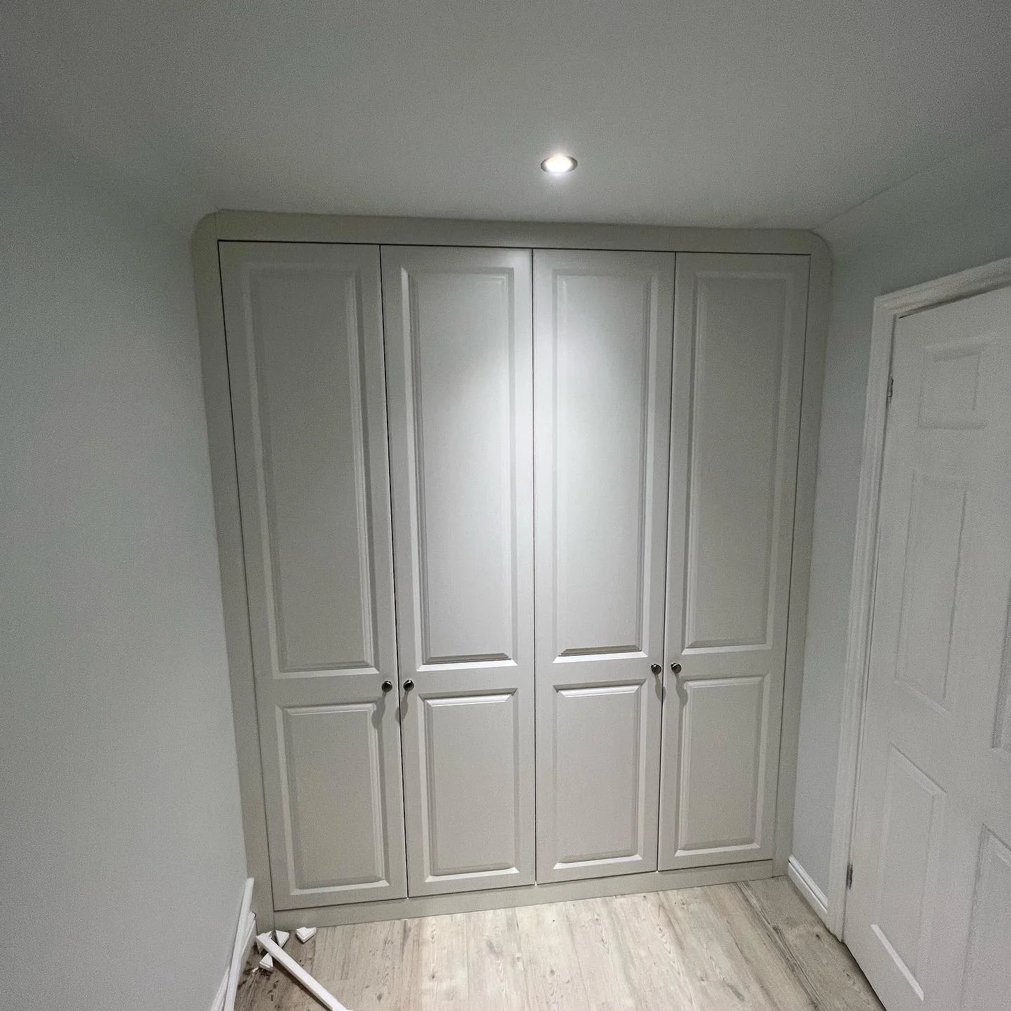 Built-in white wardrobe with four doors in a room with light wooden flooring.
