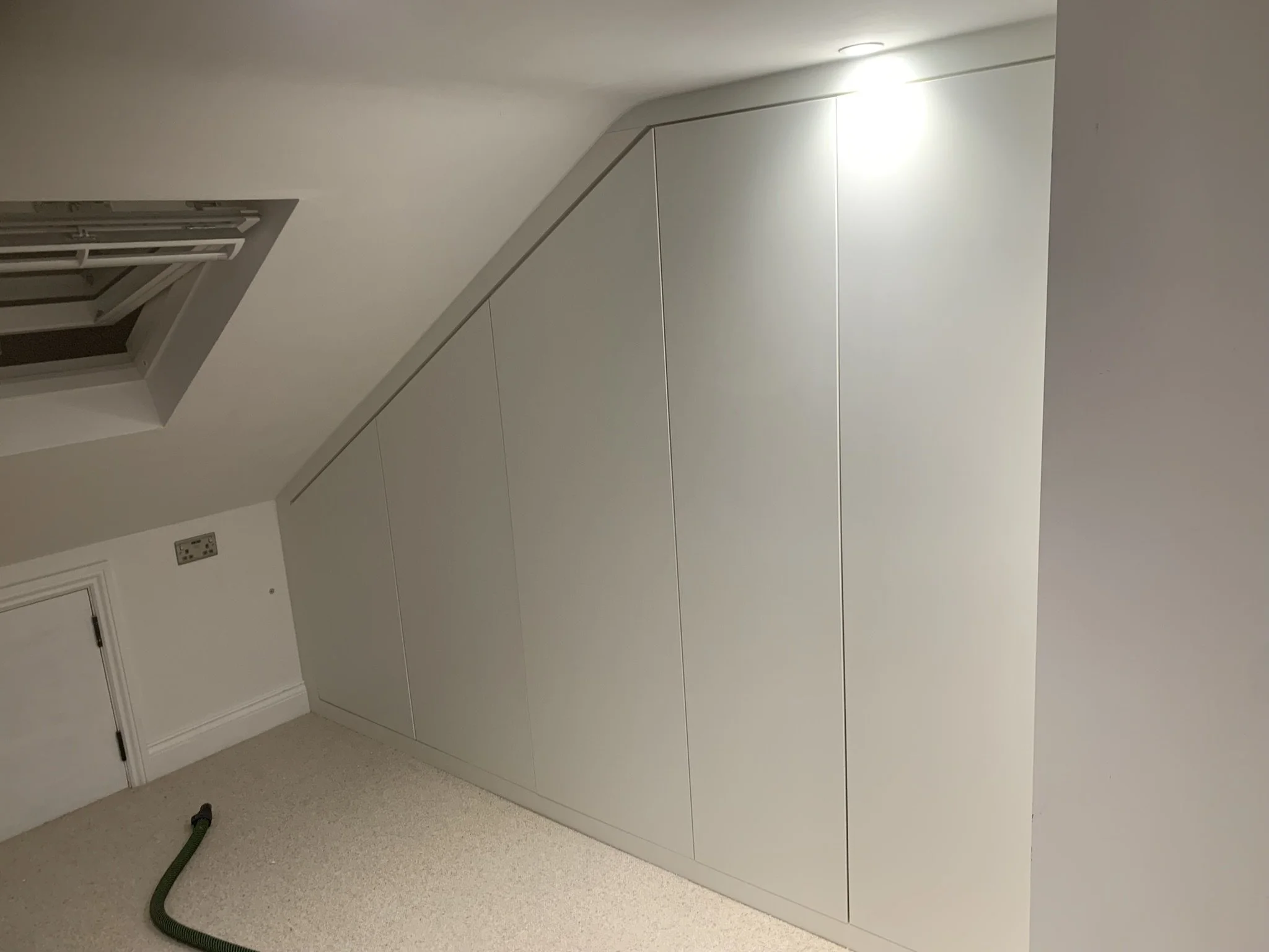 Room with sloped ceiling, in-built storage, and vacuum hose