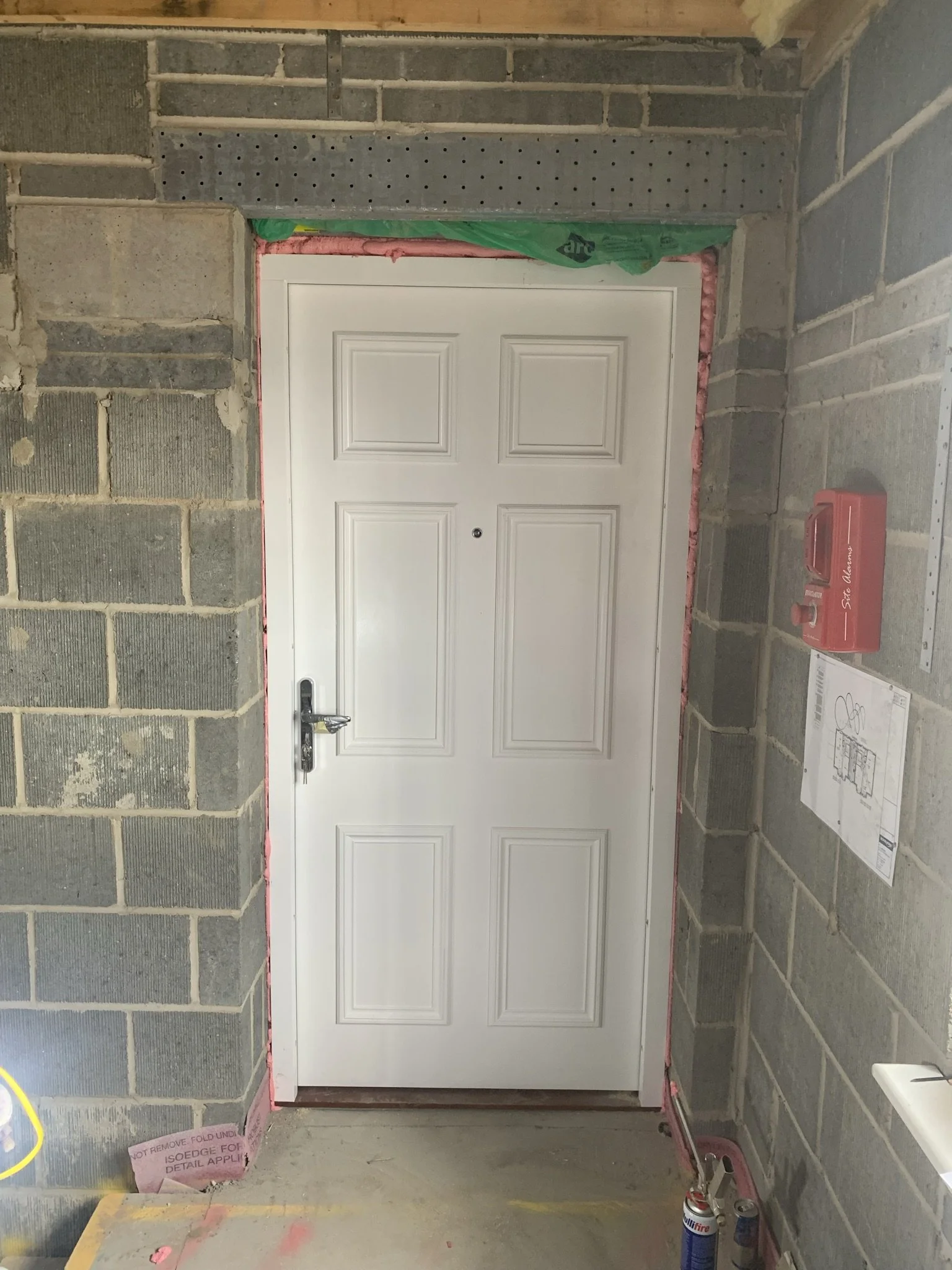 White door installed in a construction environment with unfinished brick walls and insulation around the door frame.