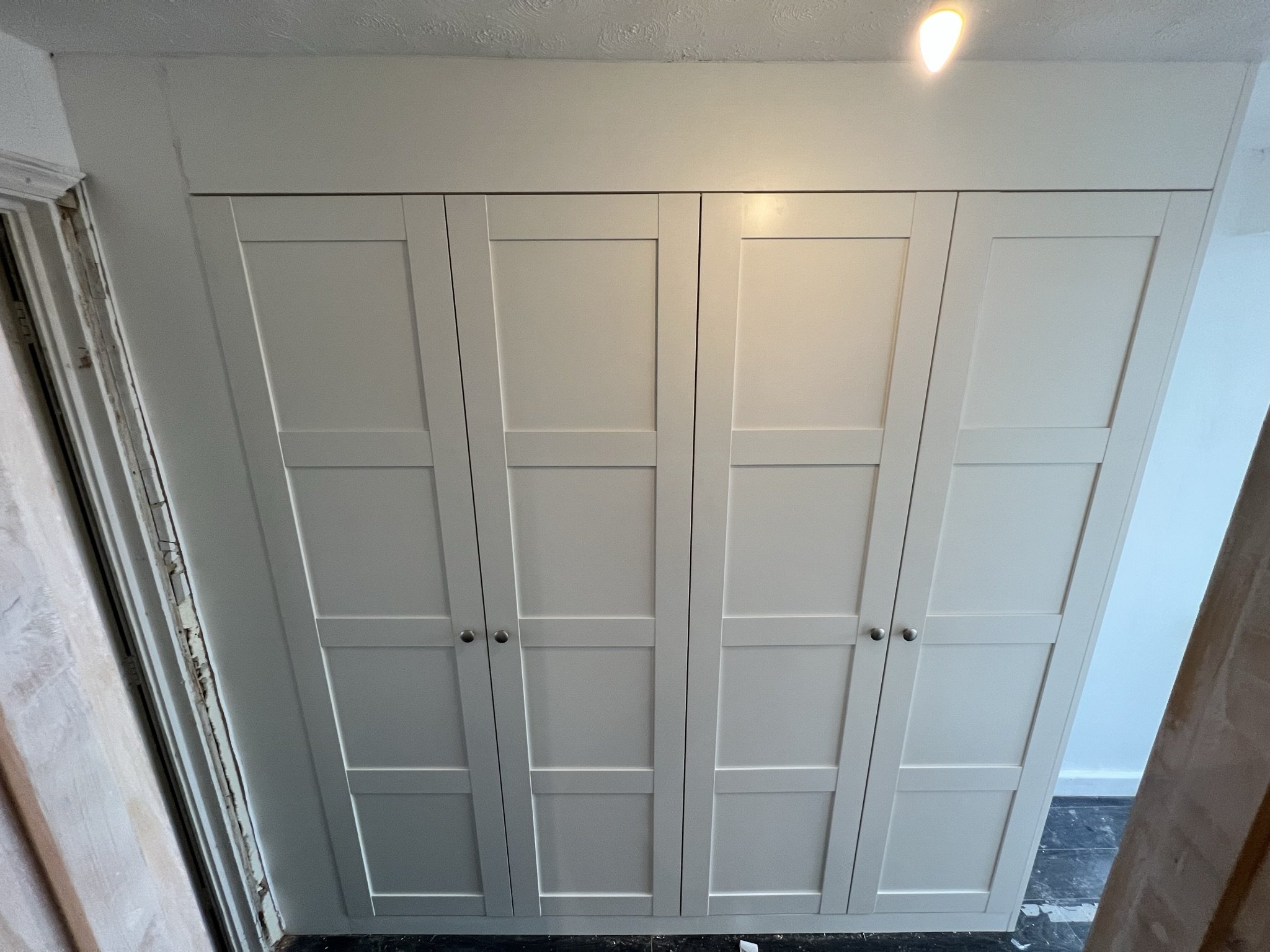 Built-in white wardrobe with four doors and recessed lighting.