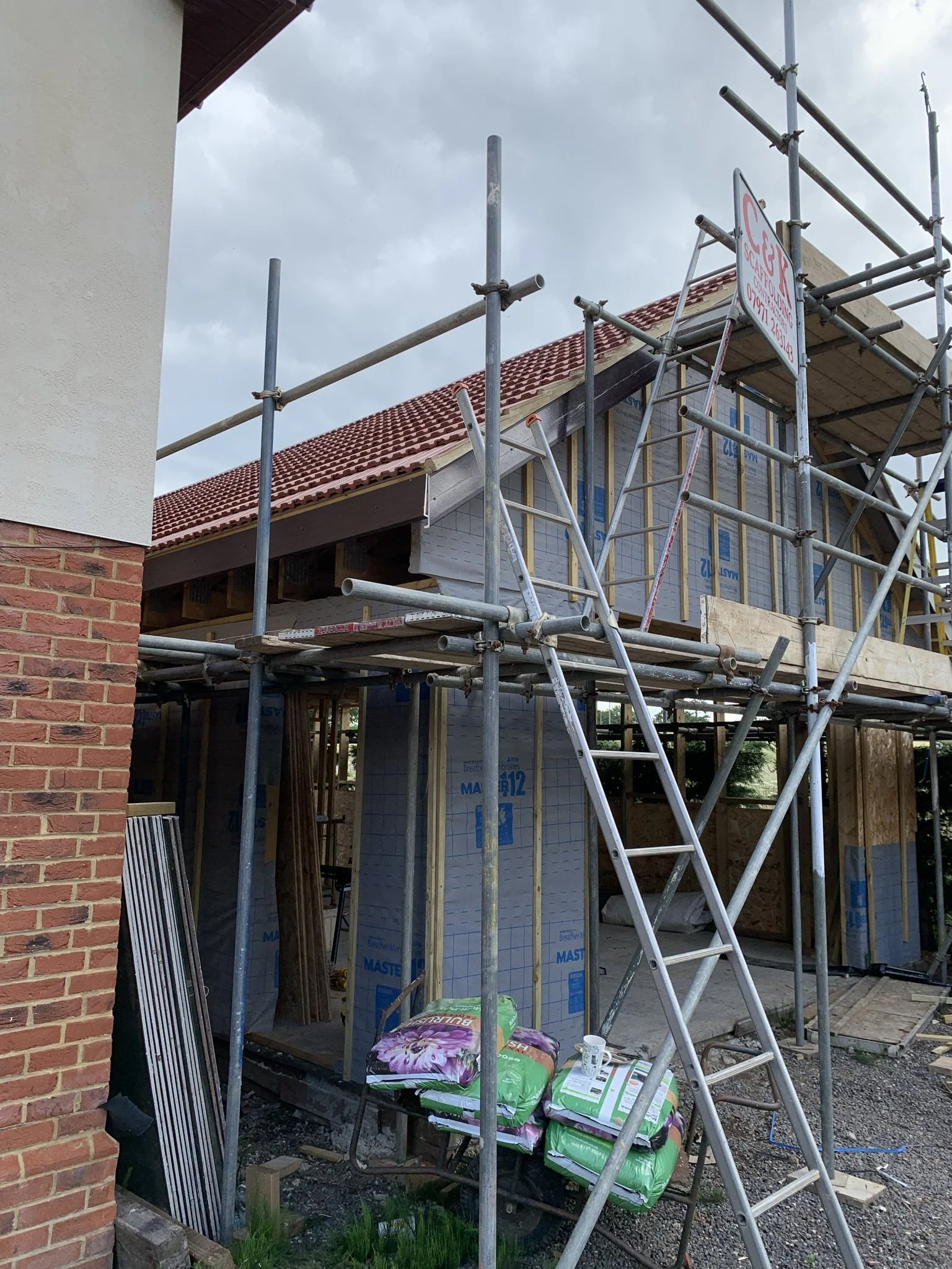 Construction site with scaffolding and a partially built house, showing brick walls and roofing materials.