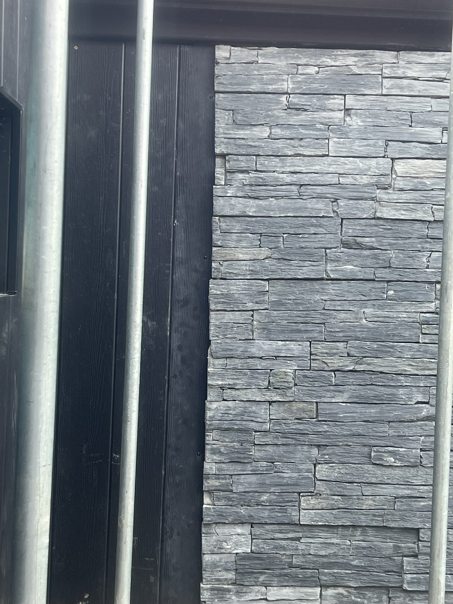 Close-up of a black wooden wall with two metal pipes and a gray stone brick wall adjacent to it.