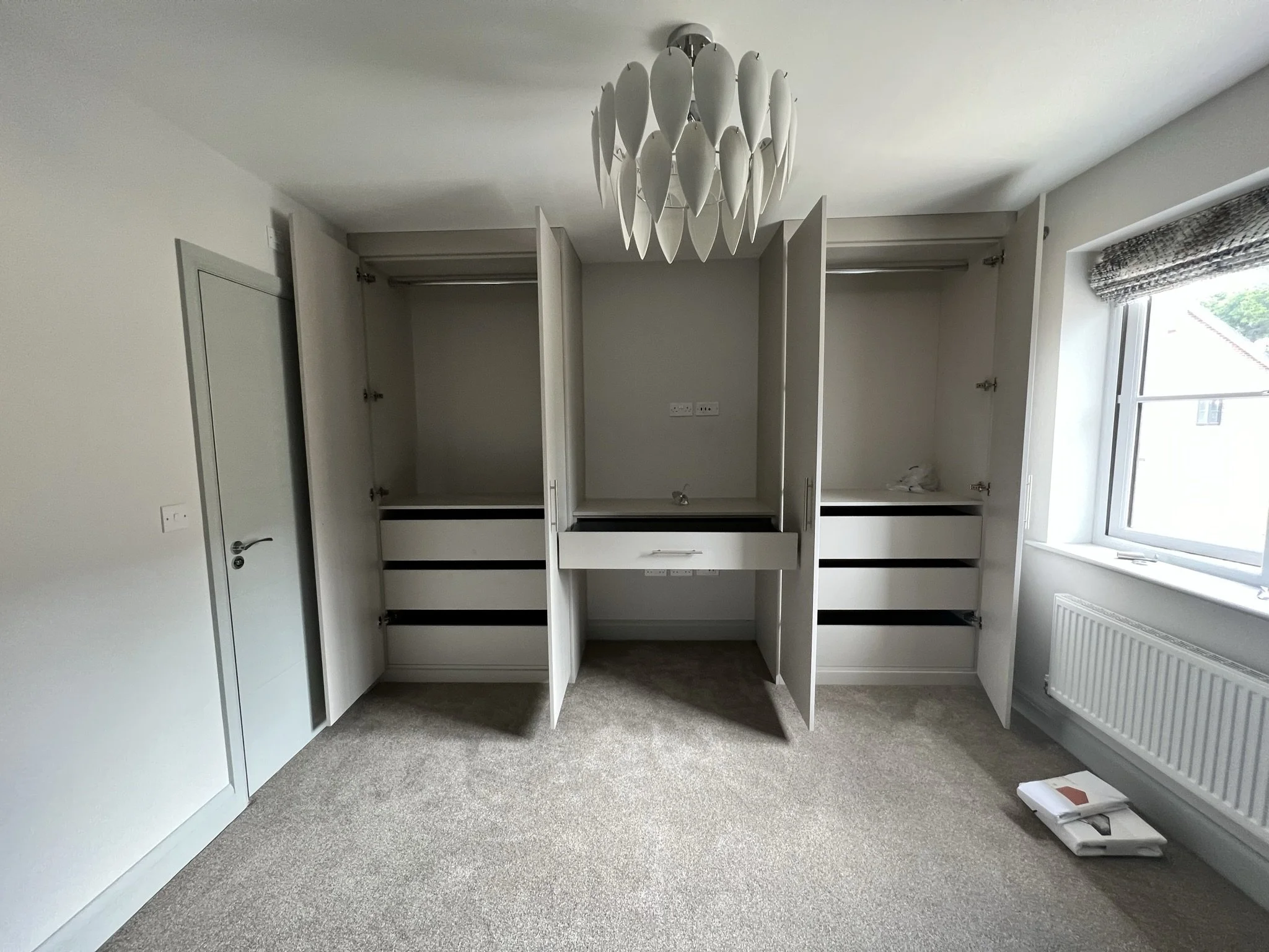 Interior of a room with open closets, drawers, a light fixture, and a window.