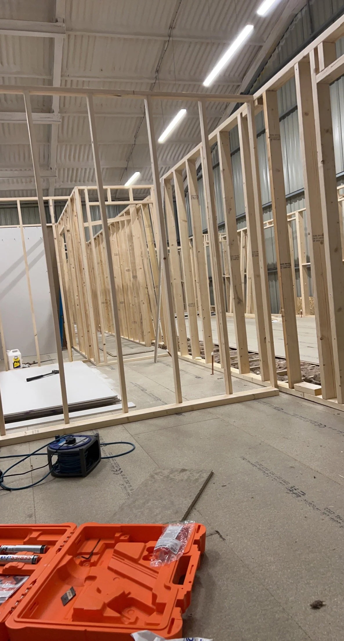 Construction site with wooden framing in a warehouse, tools and cables on the floor.