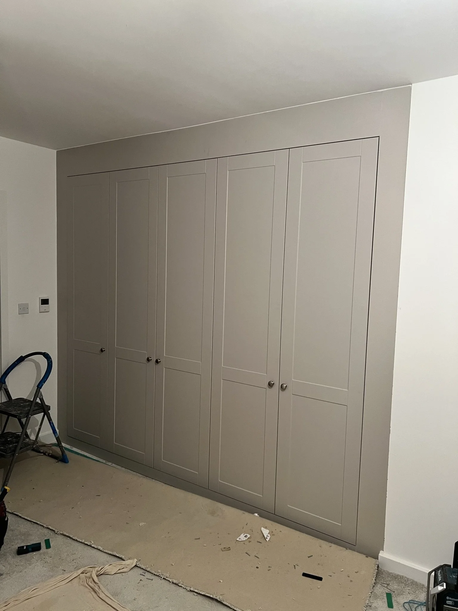 Built-in wardrobe with closed doors, beige color, in a room under renovation with a ladder and scattered materials on the floor.