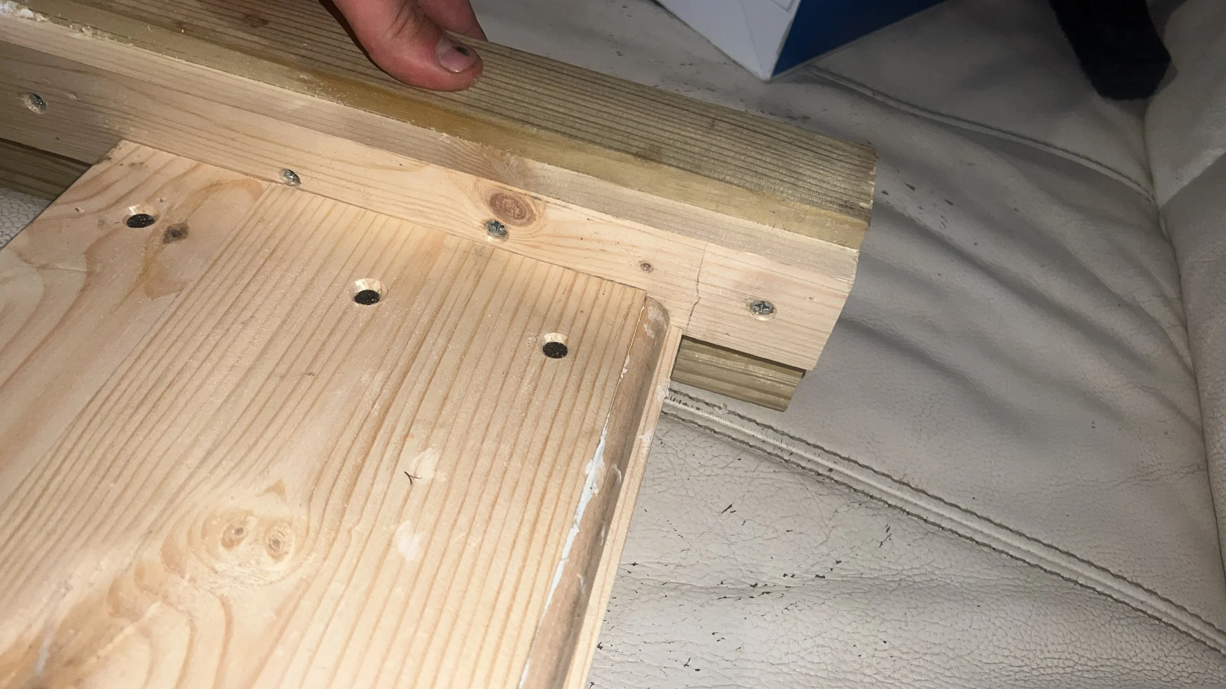 Close-up of joined wooden planks with screws, showing carpentry work on an upholstered surface.