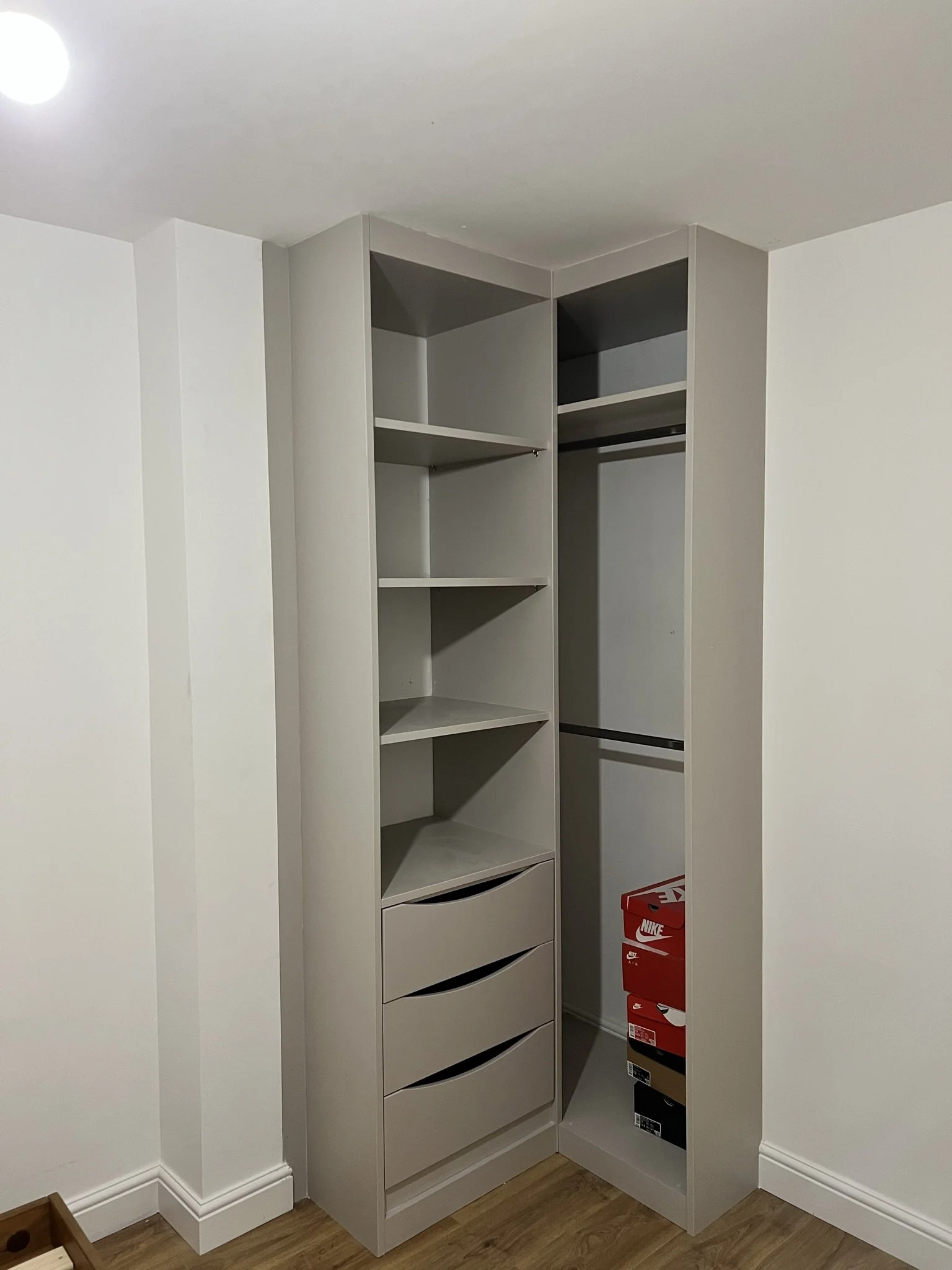 Corner wardrobe with open shelving and drawers, containing stacked Nike shoe boxes, in a room with a wooden floor.