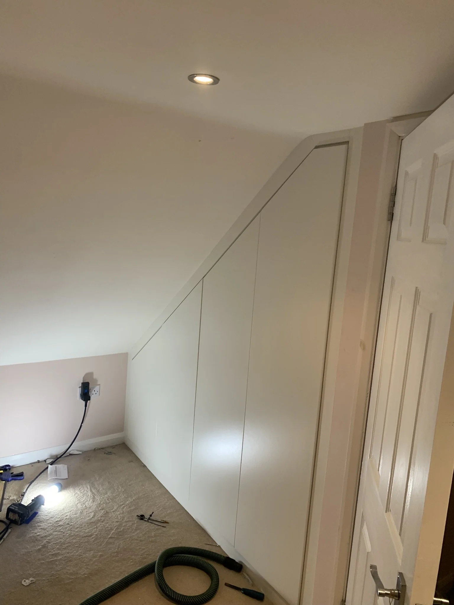 Sloped ceiling room with custom-built cabinetry and tools on the floor.