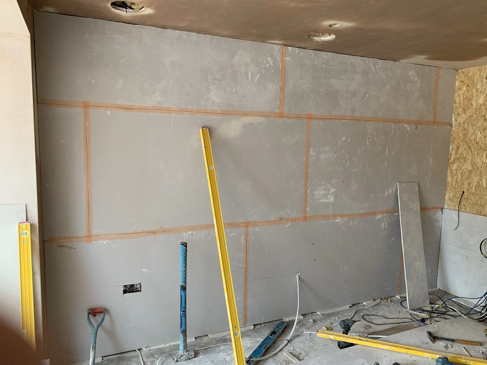Construction site with drywall installation, yellow level tools, and construction materials on the floor.