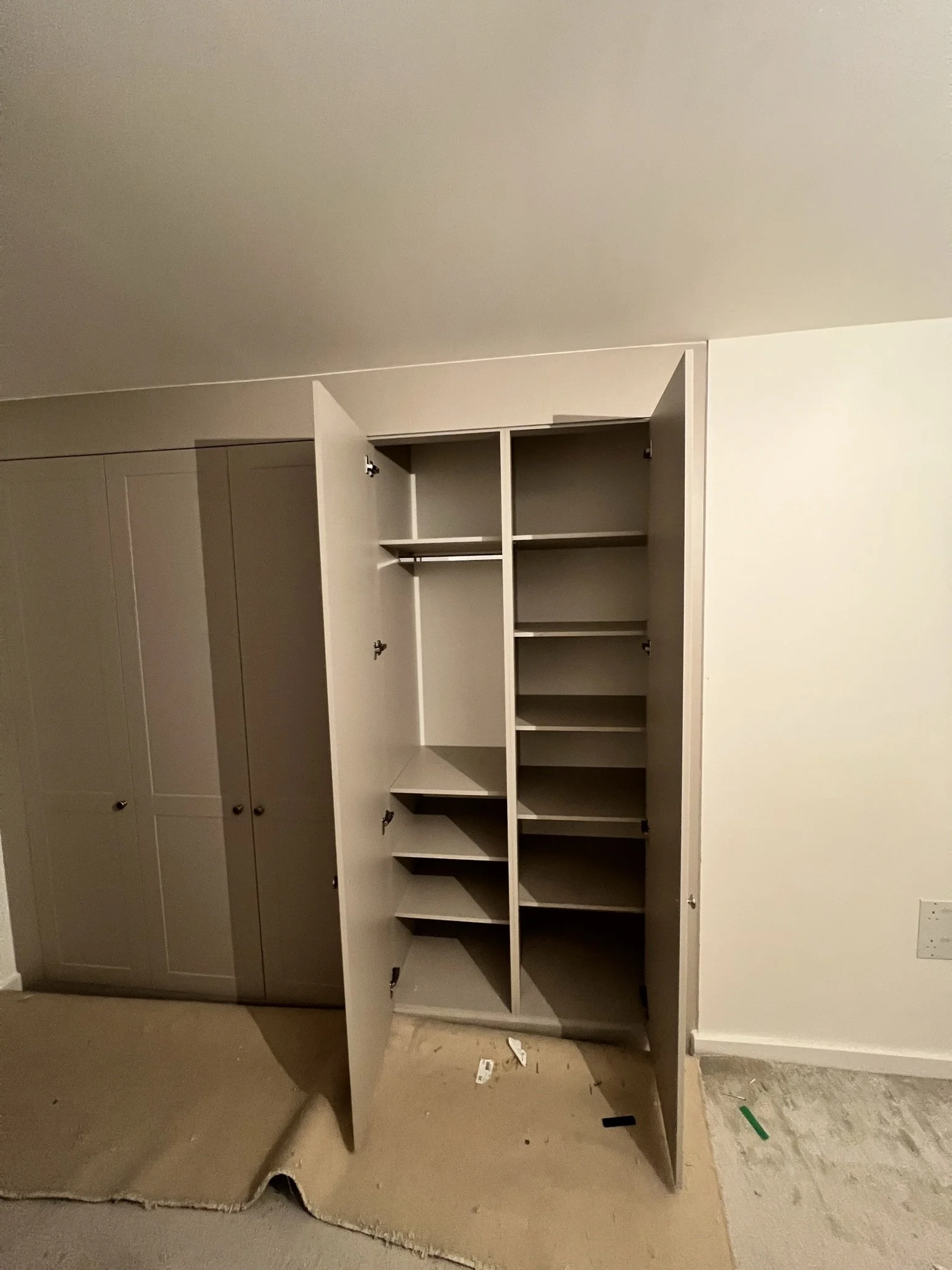 Open wardrobe with shelves in a room with a light-colored carpet partially pulled up.
