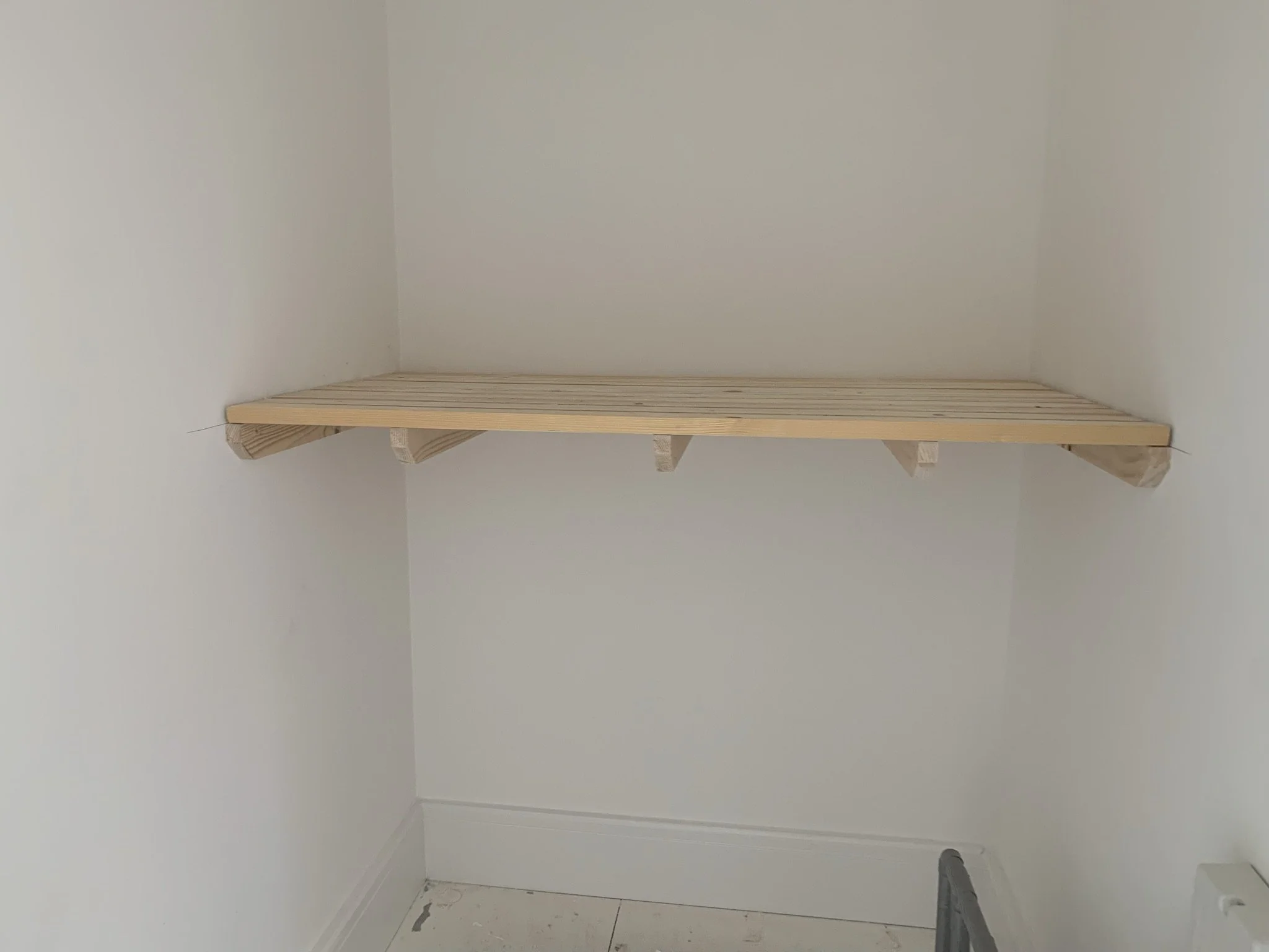 Empty closet with a wooden shelf installed.