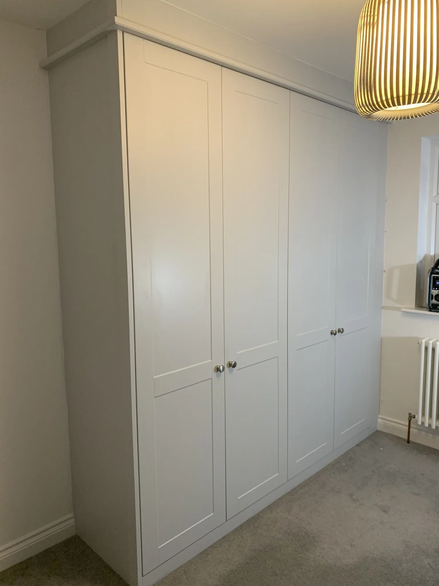 White wardrobe with three doors and silver knobs in a room with carpet and a modern pendant light.