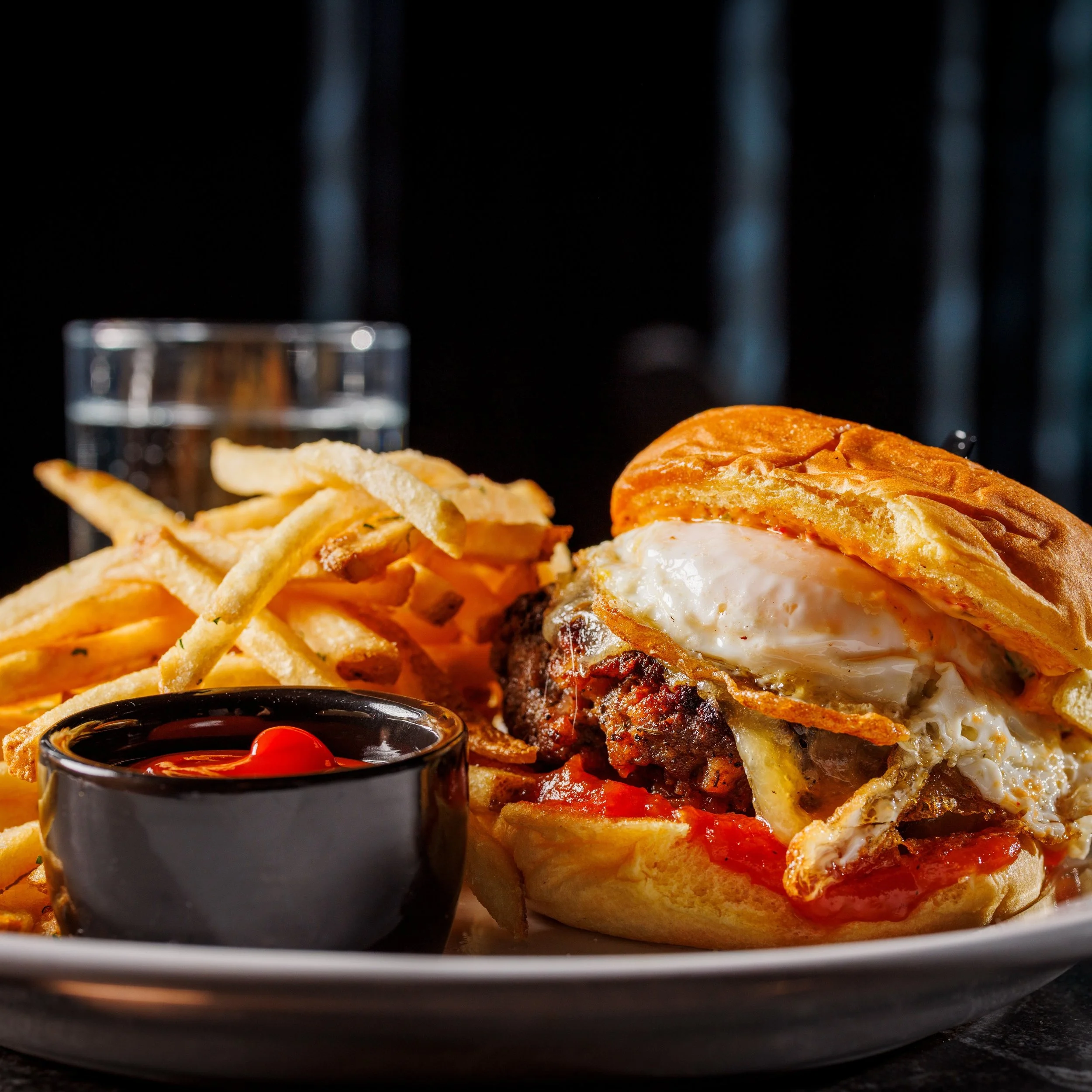 Happy Hour at The Saint, featuring our Texas Bison Burger, with Nueske's Applewood Bacon crust, Fried Egg, Gouda , and Tomato Jam. Also available during Brunch!