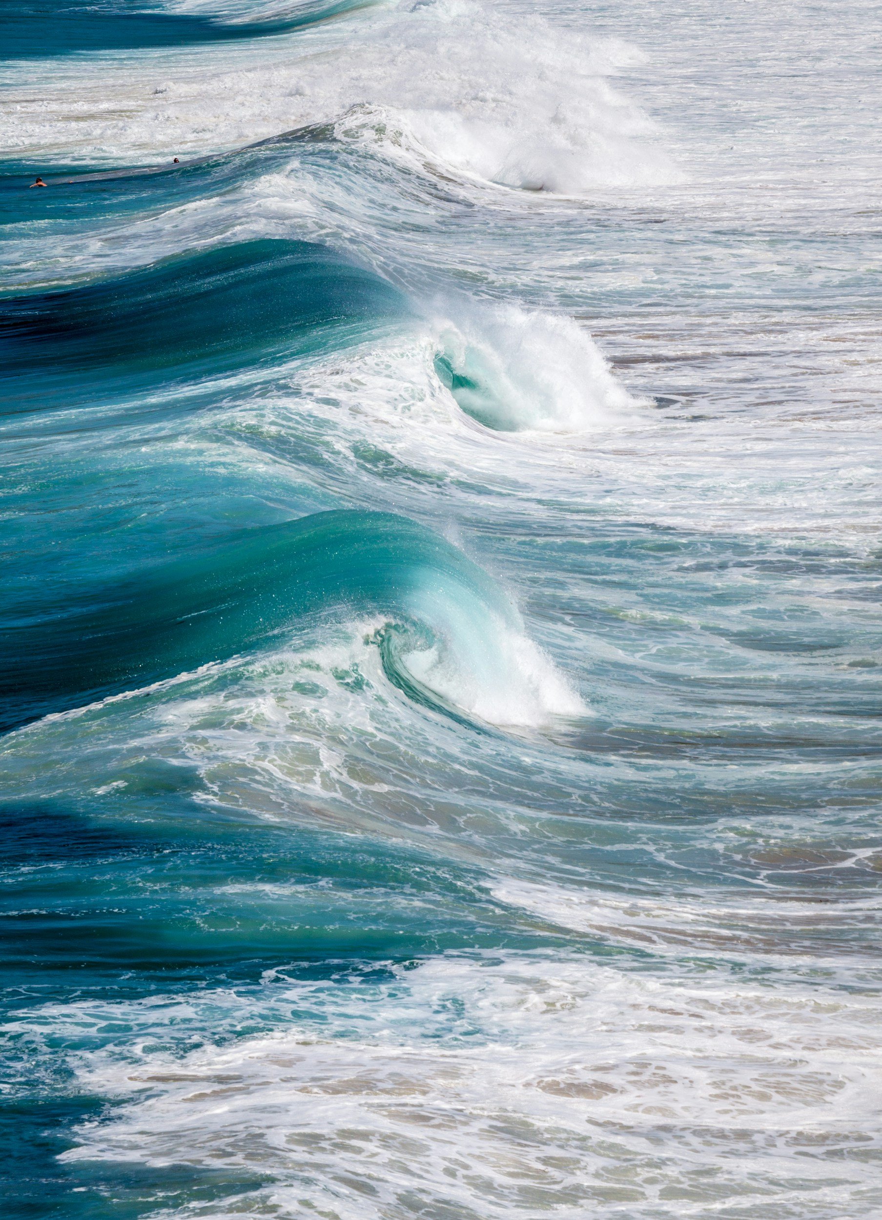 Ocean waves with white foam and blue water under a partly cloudy sky