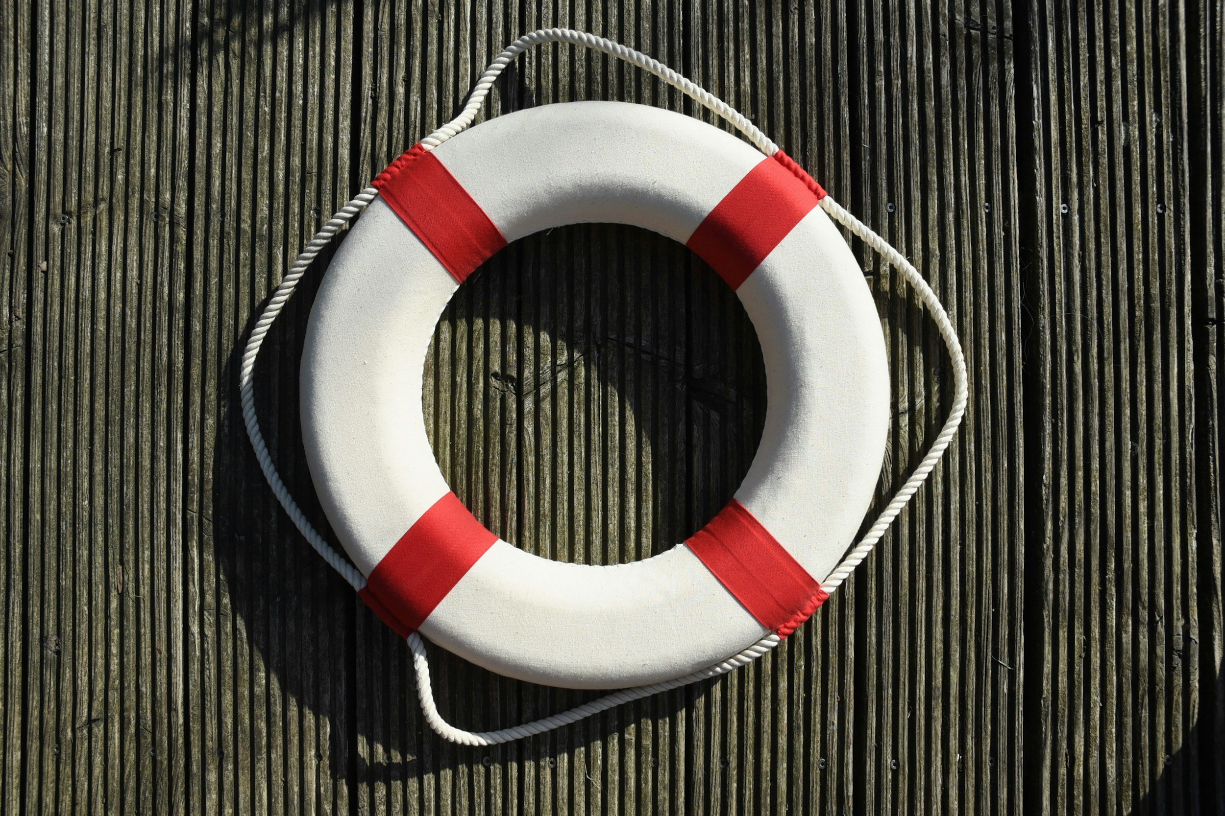 A white life preserver with red stripes and a rope around it, placed on a wooden surface.