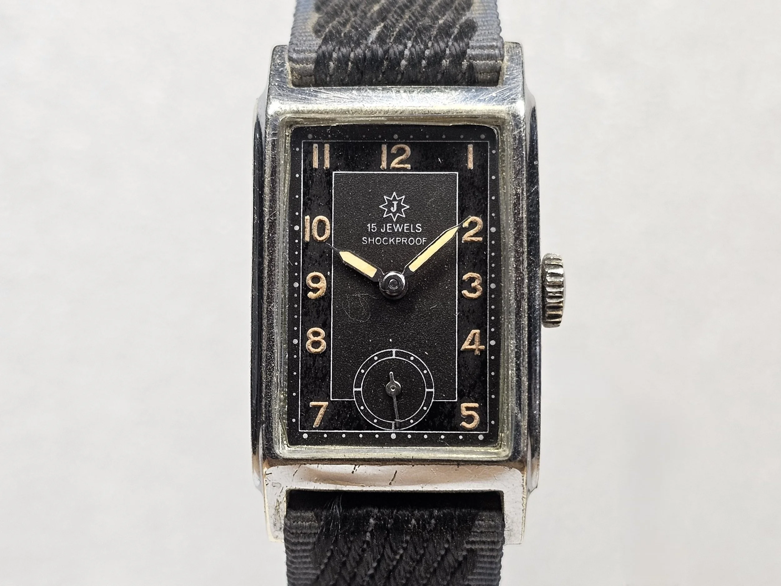 1950s Junghans tank-style dress watch with black gilt dial, sub-seconds register, and chrome-plated rectangular case on black textile strap