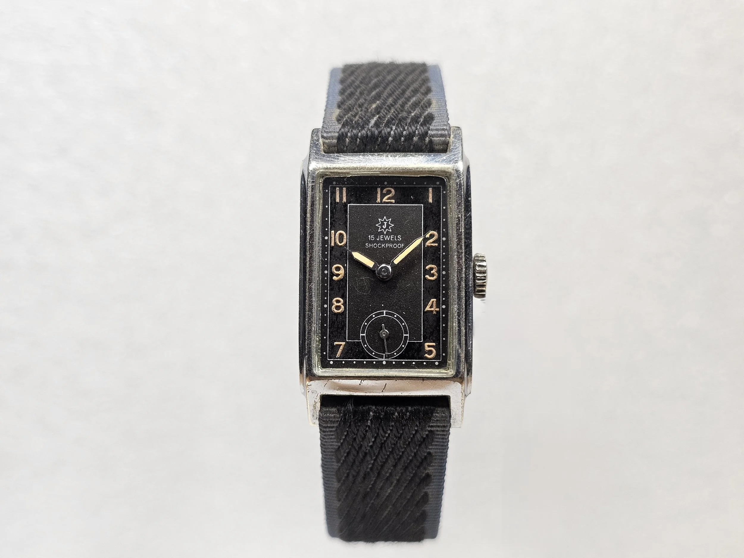 1950s Junghans tank-style dress watch with black gilt dial, sub-seconds register, and chrome-plated rectangular case on black textile strap