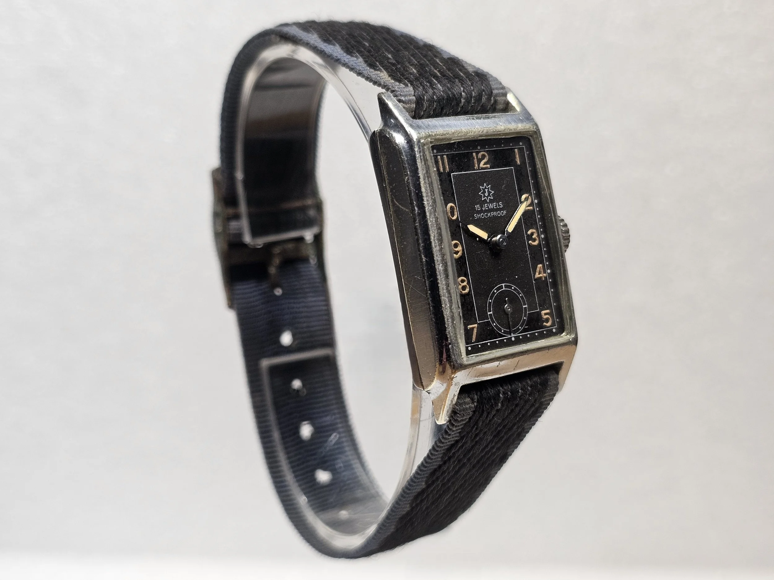 1950s Junghans tank-style dress watch with black gilt dial, sub-seconds register, and chrome-plated rectangular case on black textile strap