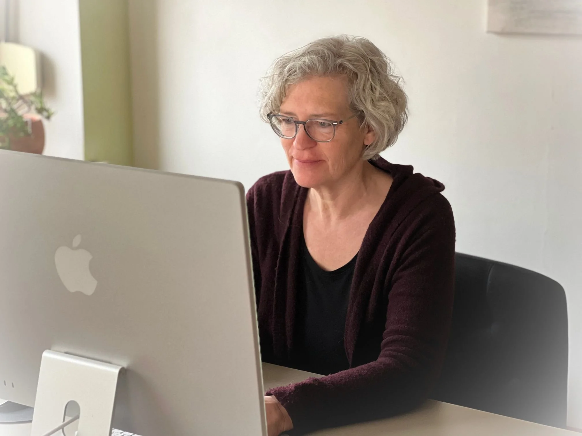 Ältere Frau mit Brille arbeitet am Computer in einem Büro.