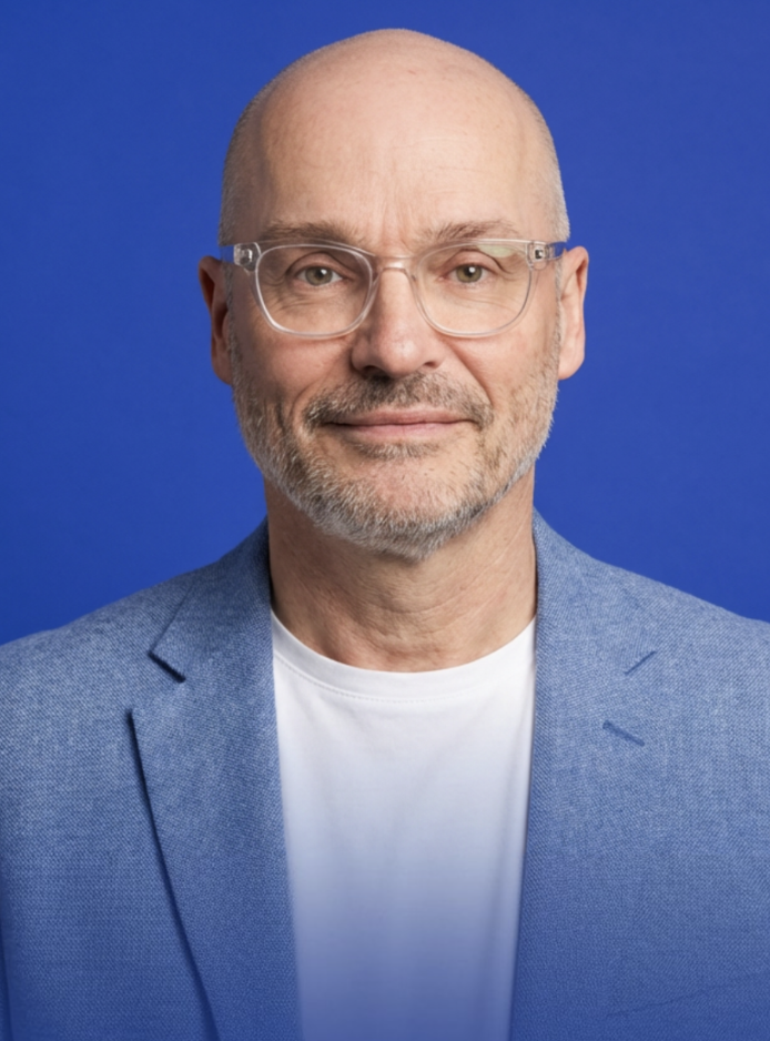 Headshot of Peter Sykes wearing a blue jacket against a blue background.