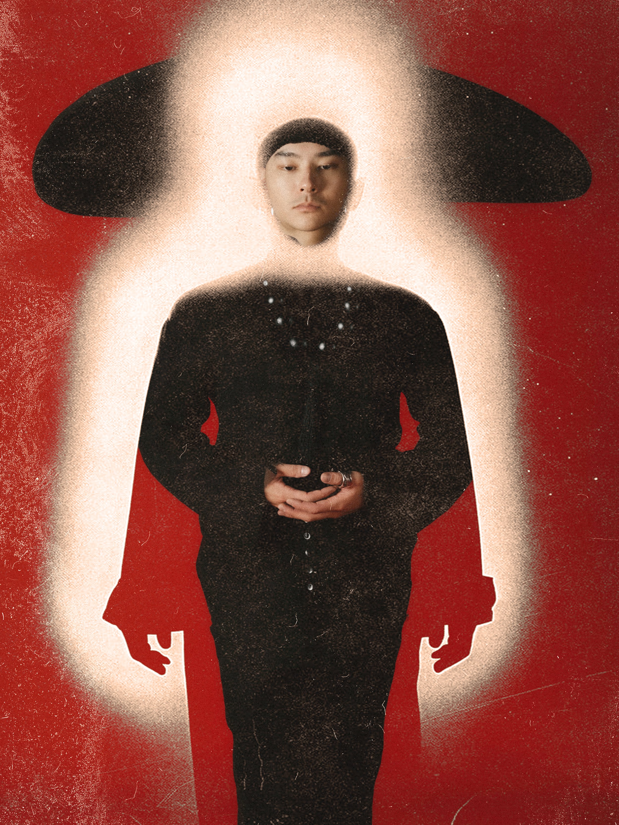 A woman wearing a black dress with her hands clasped in front of her, standing in front of a red background. The woman's face is surrounded by a large, black hat with a wide brim.