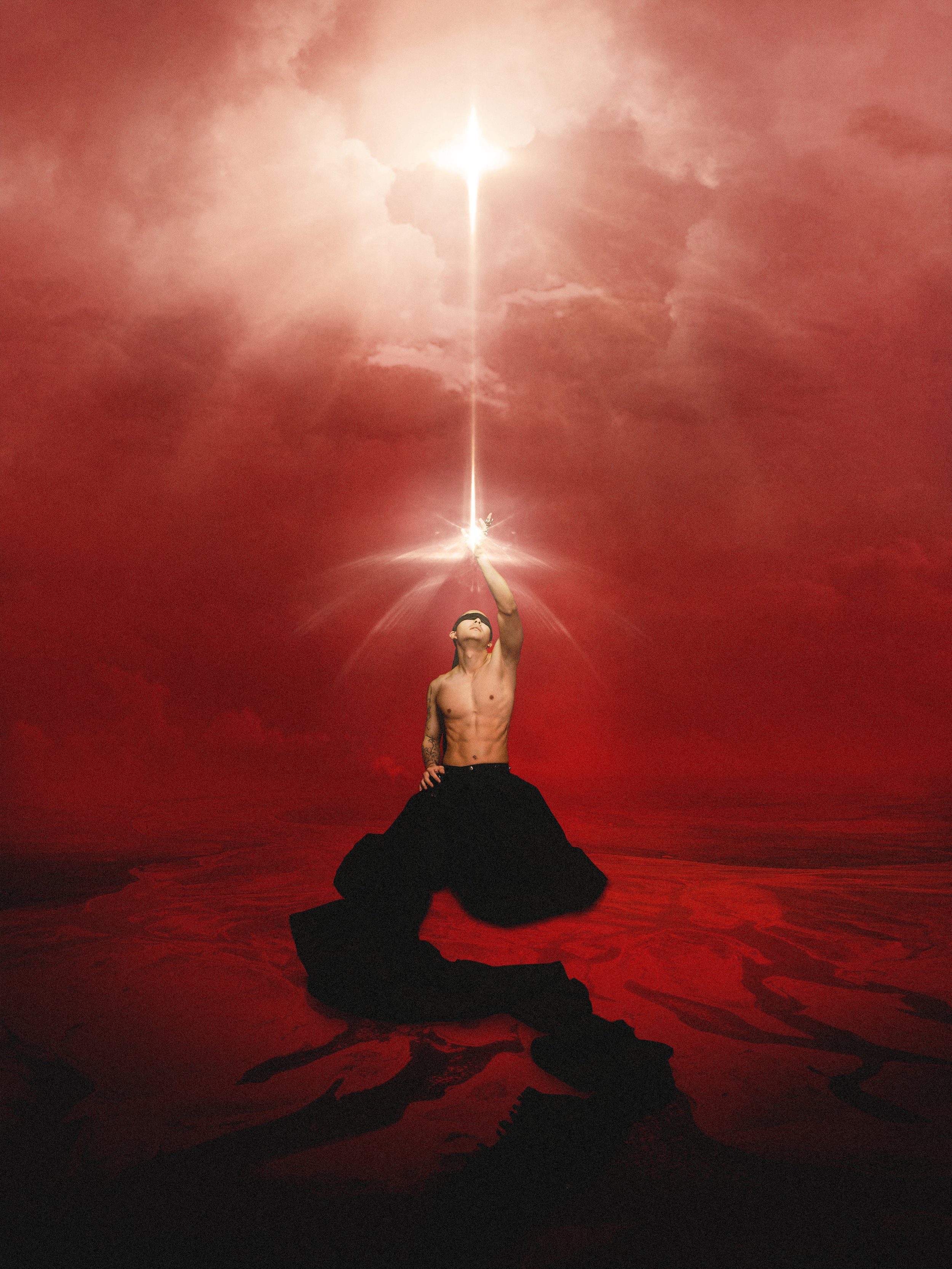 A shirtless man wearing black pants kneeling on the ground, pointing upward with his right hand, with a bright light or flame emanating from his finger, against a background with dark clouds and red ground.