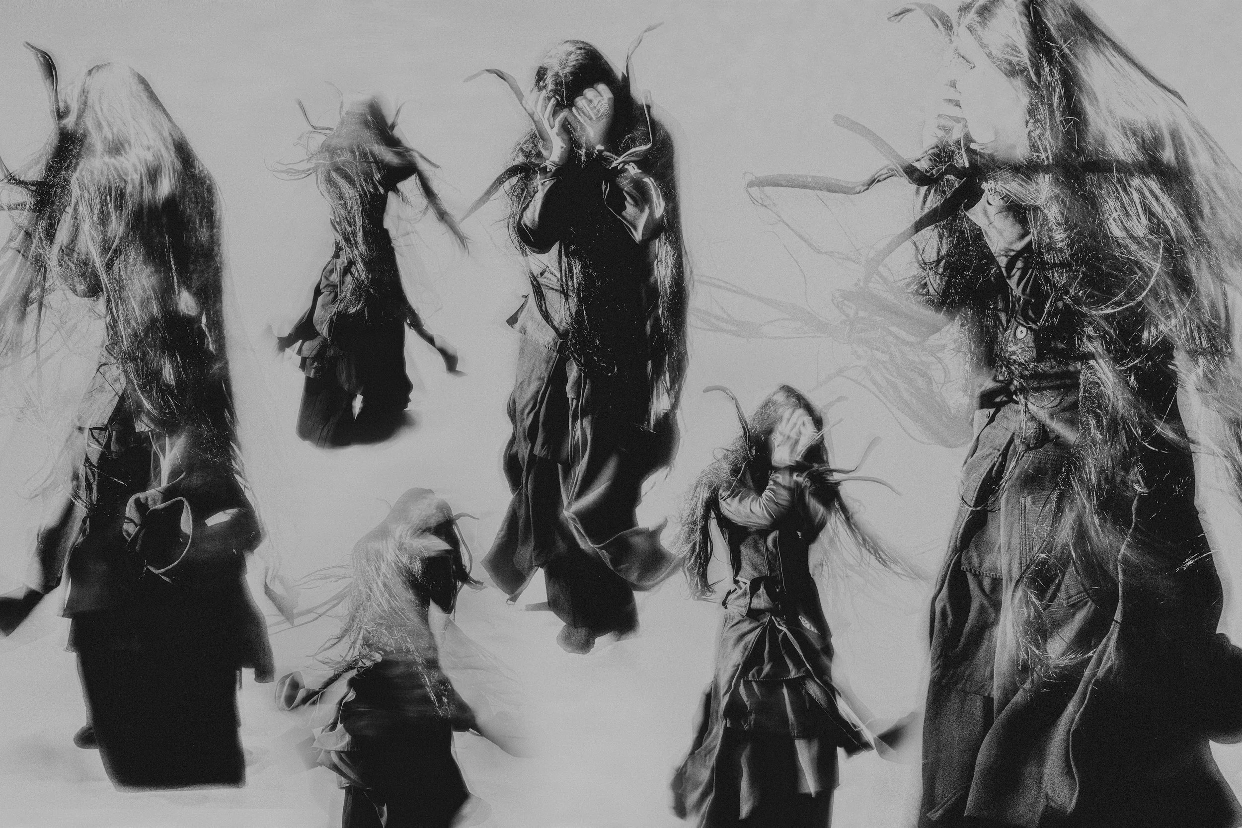 Black and white photograph of several people engaged in a dance or physical activity, with some individuals in motion and others standing still, against a plain background.