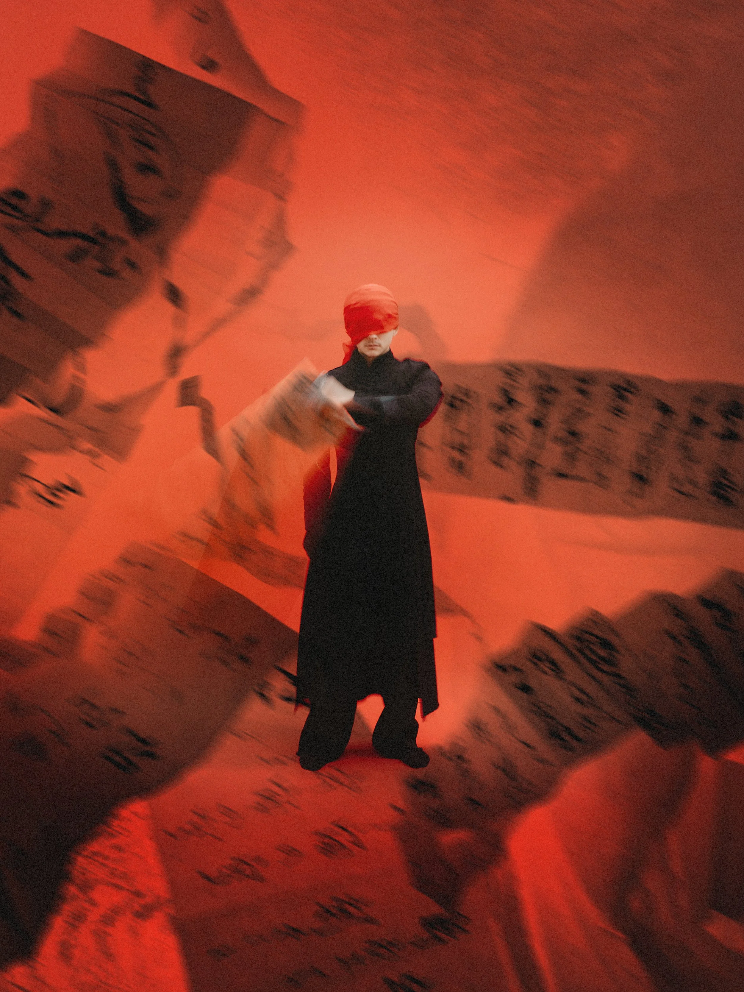 Person wearing a red blindfold and black clothing, standing against a red background surrounded by torn posters with Asian script.