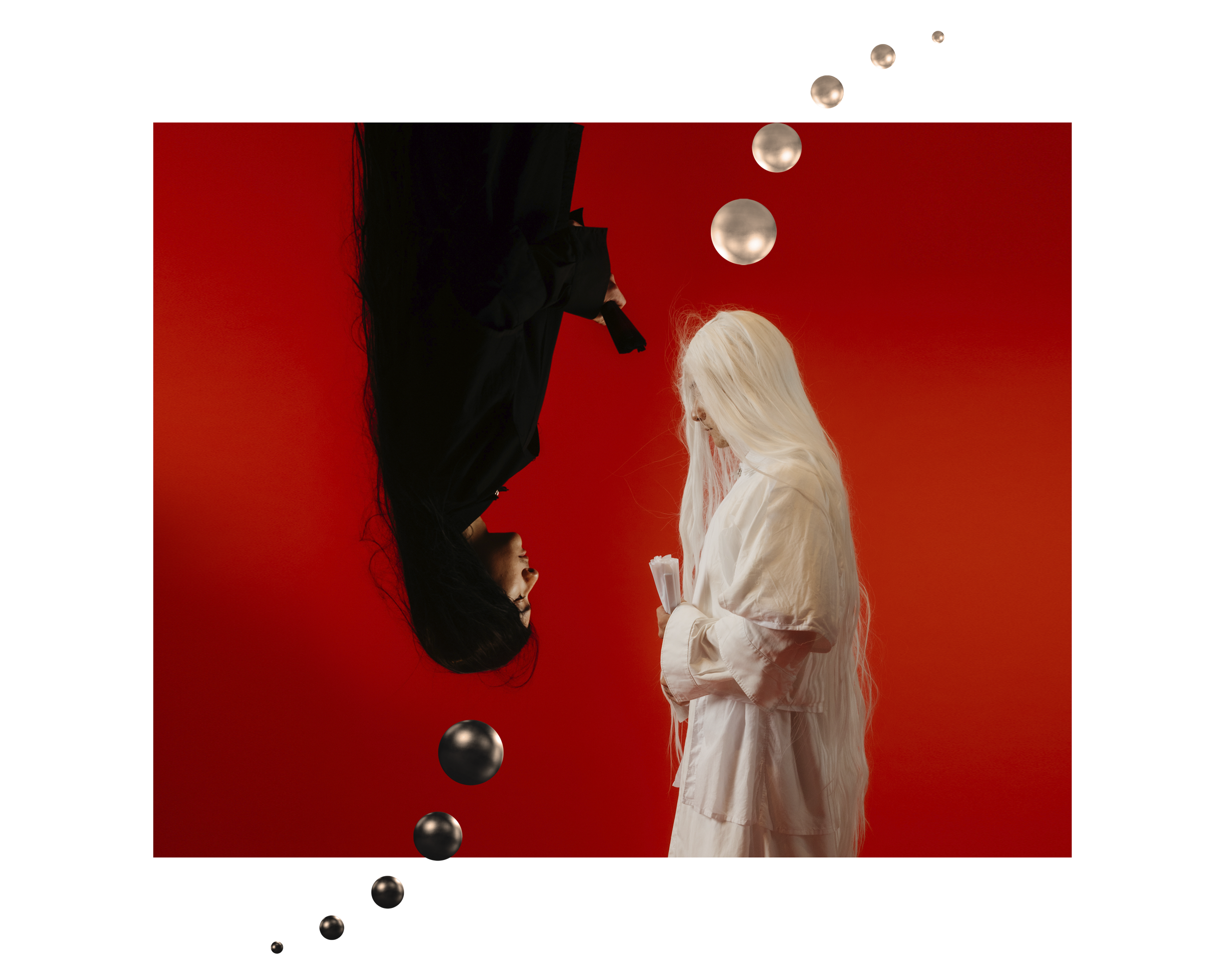 A woman in a white dress holding papers or a book, with a red background and black and metallic spheres suspended around her, with some spheres aligned vertically above her head.